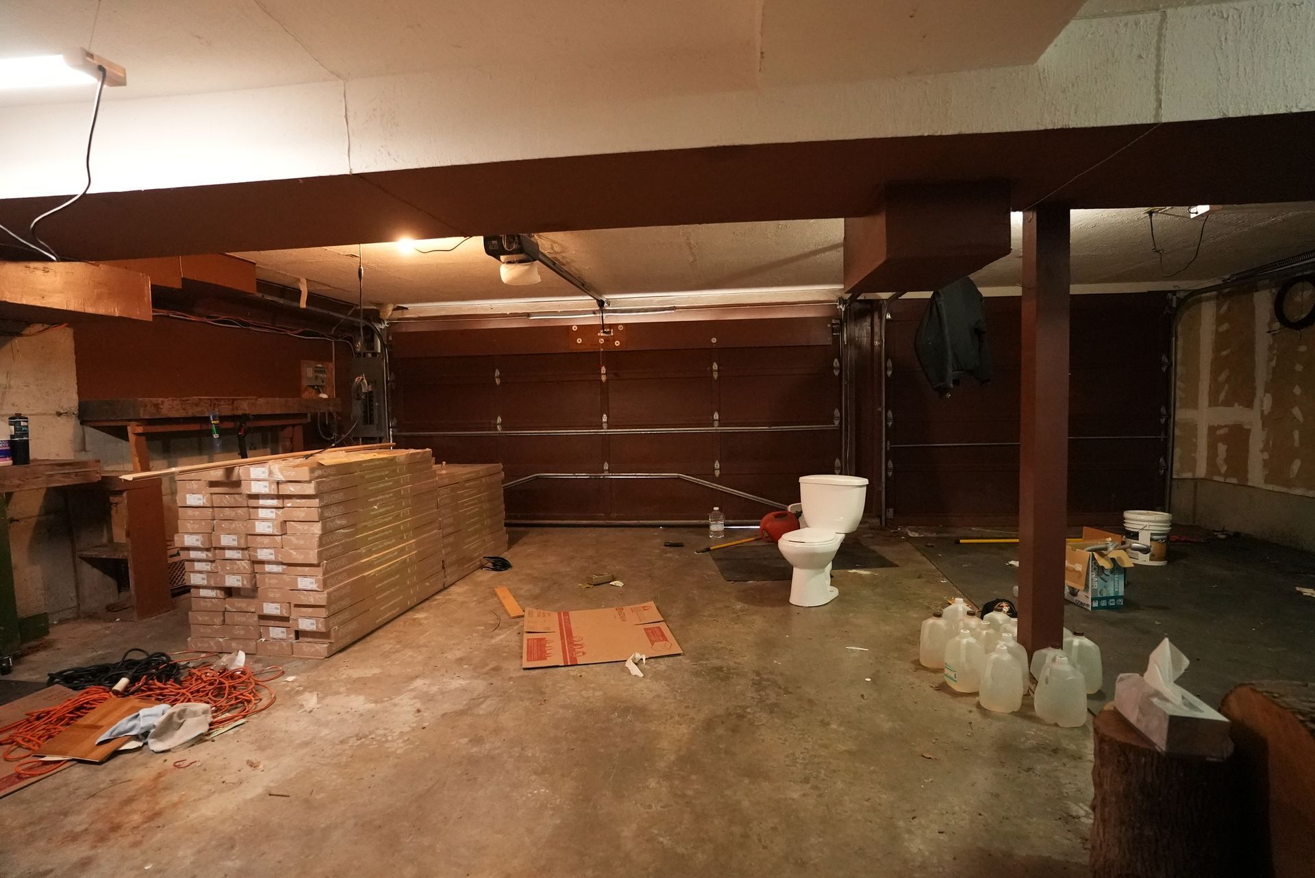 Cluttered basement with stacked boxes, scattered items, and a white toilet amid dim lighting.