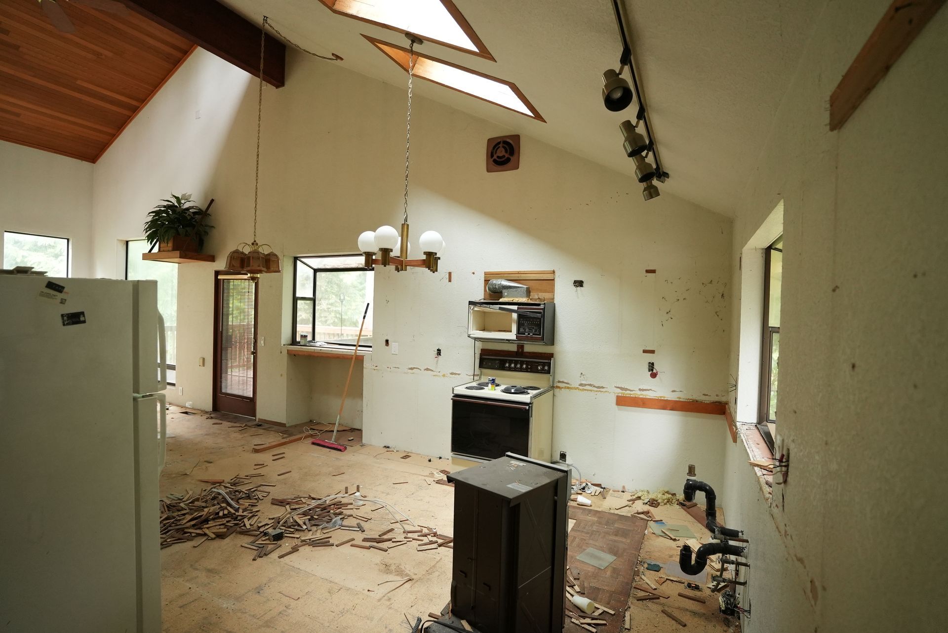 Abandoned room with debris on the floor, white walls, a cabinet, and exposed ceiling beams.
