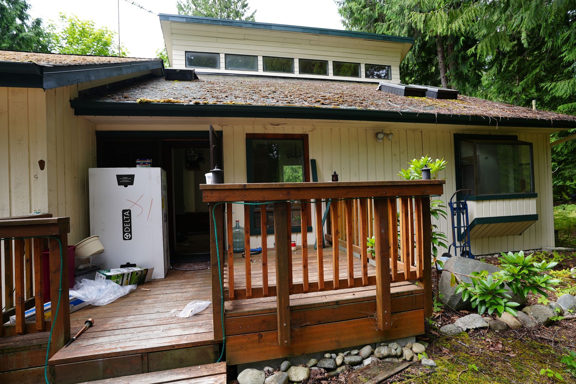 Weathered house exterior with wooden porch, railing, and white door under a mossy roof.