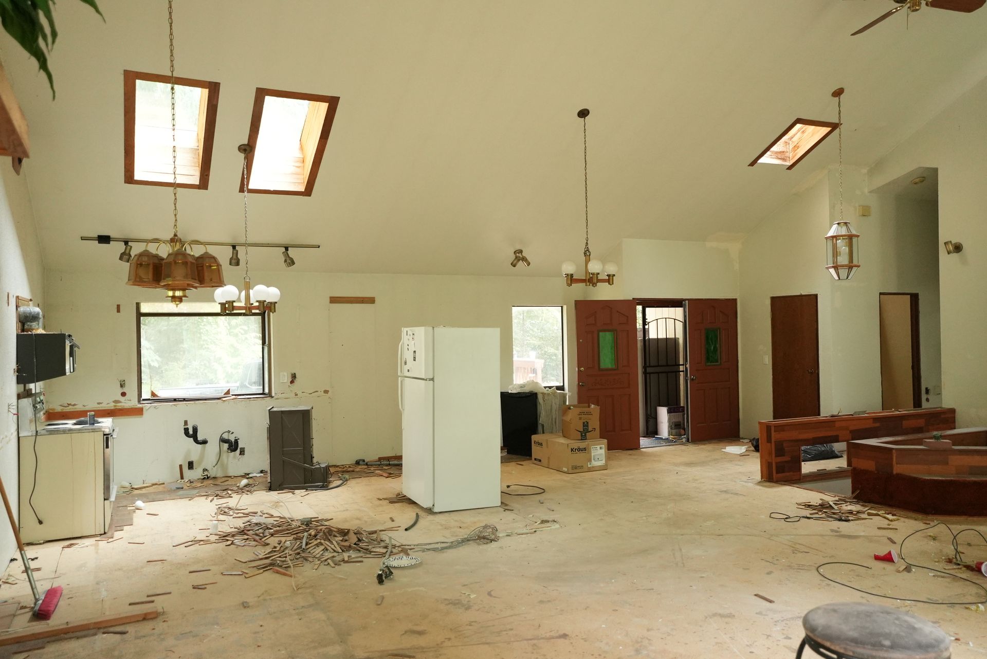 Abandoned room with debris on the floor, white walls, skylights, and scattered furniture.