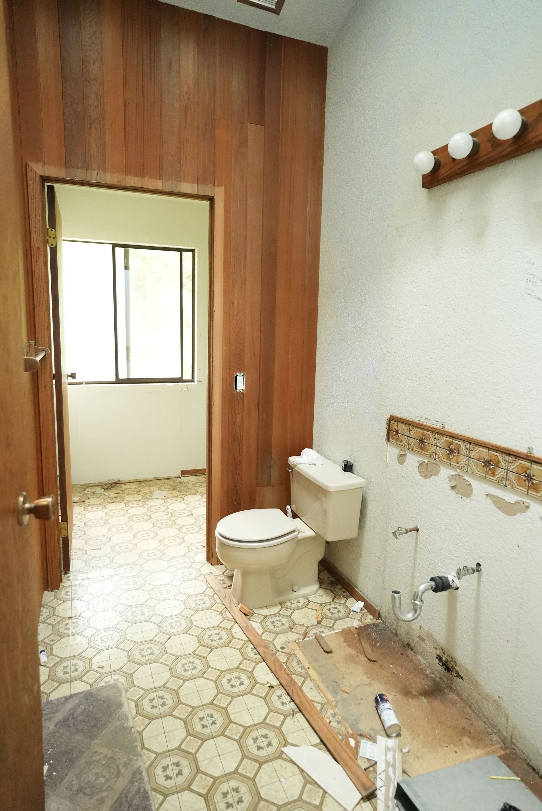 Small bathroom with toilet, sink, window, and wood-paneled wall