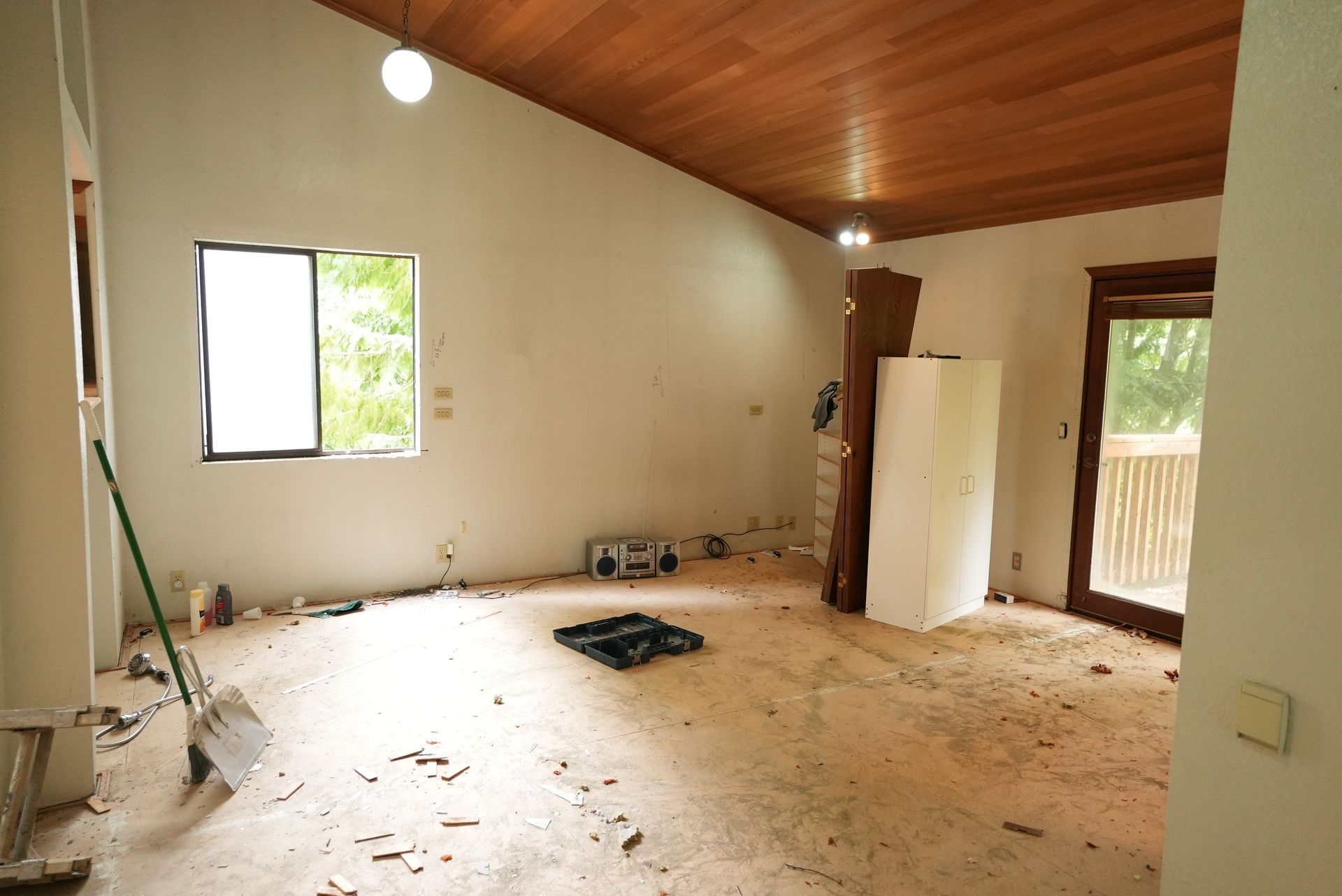 Empty room with a wooden ceiling, cream walls, scattered debris, and open windows and doorways.