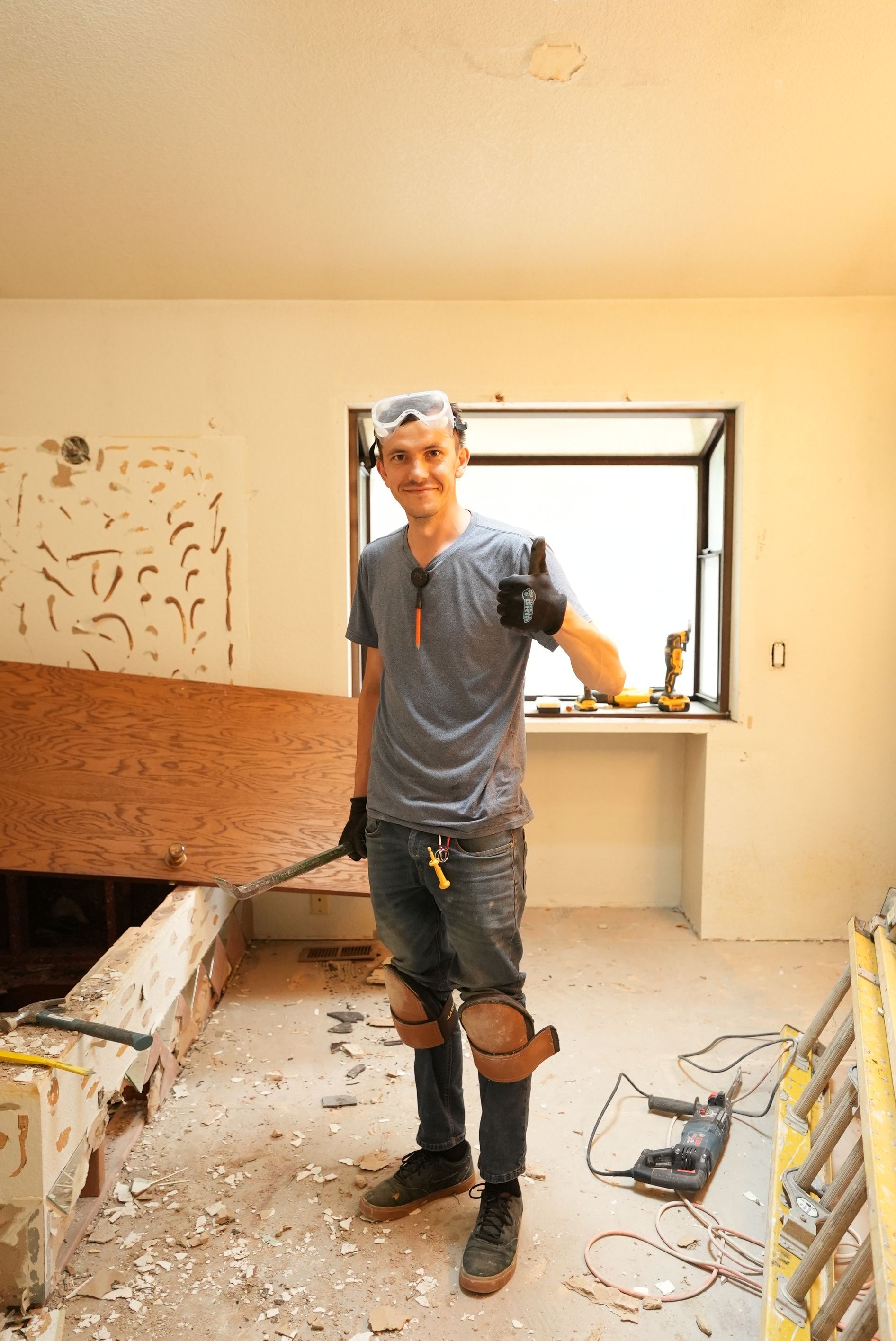 Worker standing in a room under renovation, holding a plank near an open window