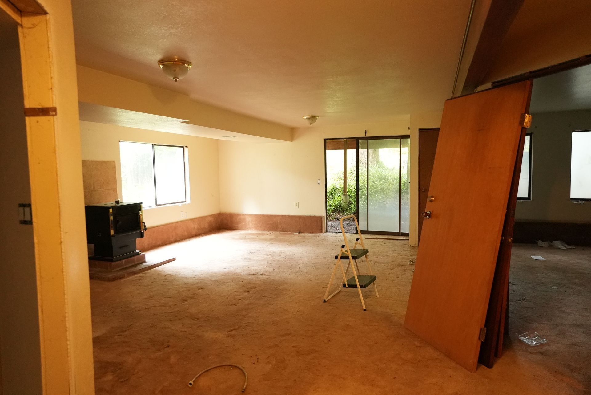 Empty unfinished room with bare walls, windows, open door, and construction materials on the floor