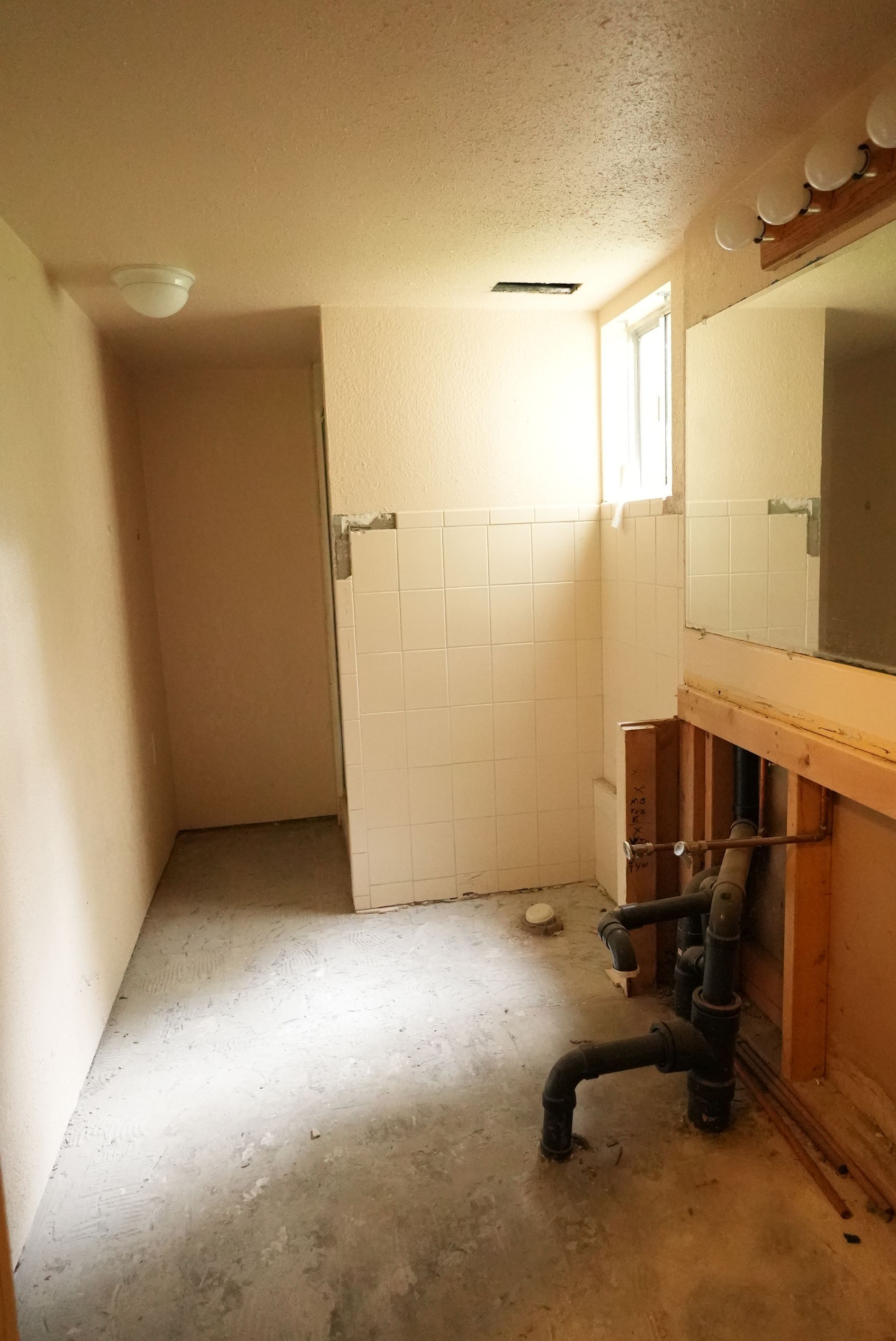 Narrow hallway with beige walls, white tiled half-wall, and a wooden cabinet with a black stool.