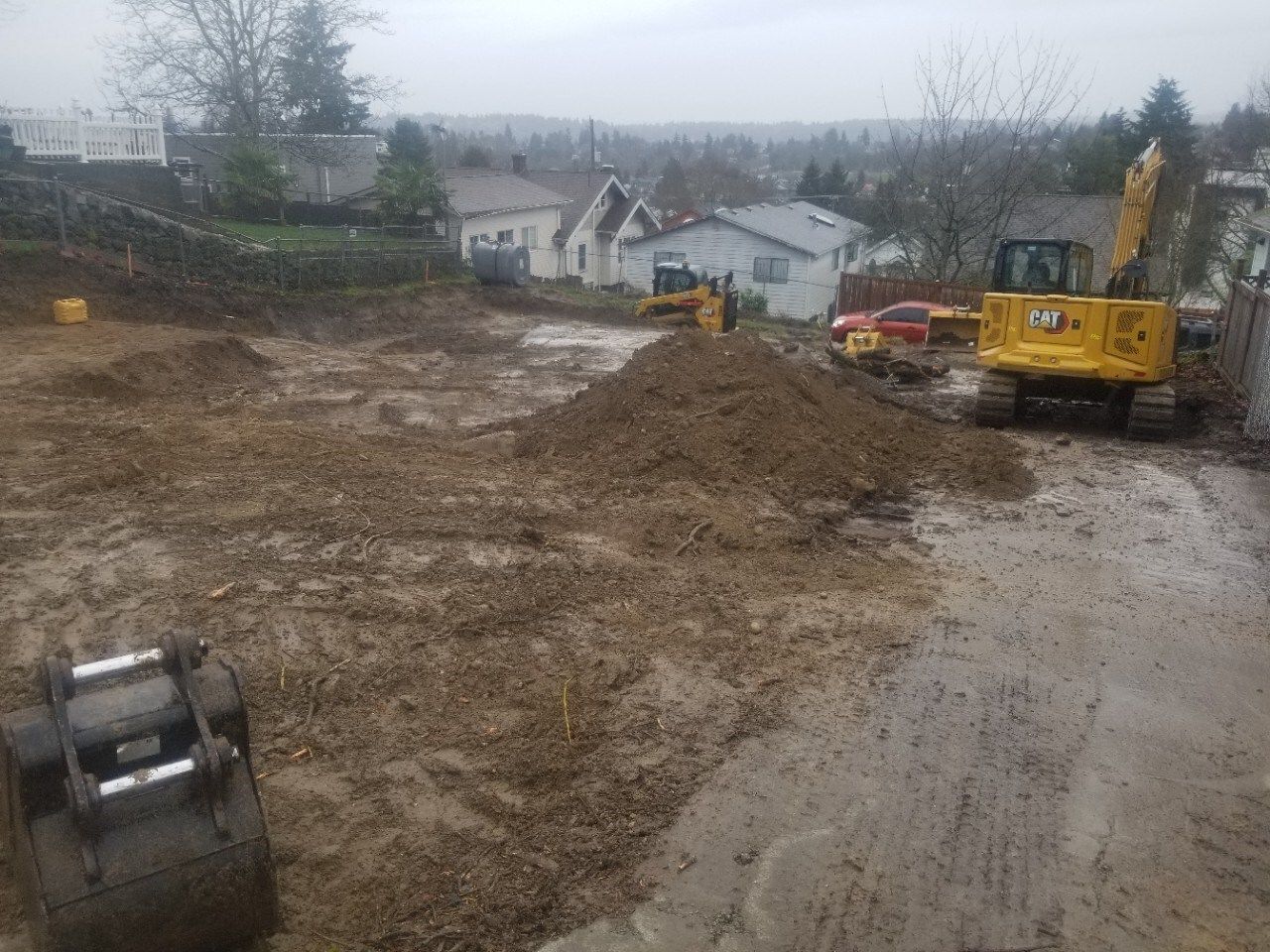 Construction site with excavators on muddy ground near houses under a gray sky