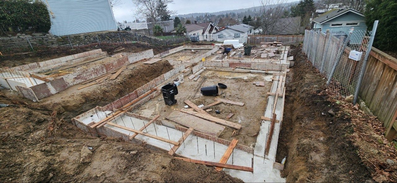 Foundation excavation site with wooden forms, rebar, and muddy ground in a residential area