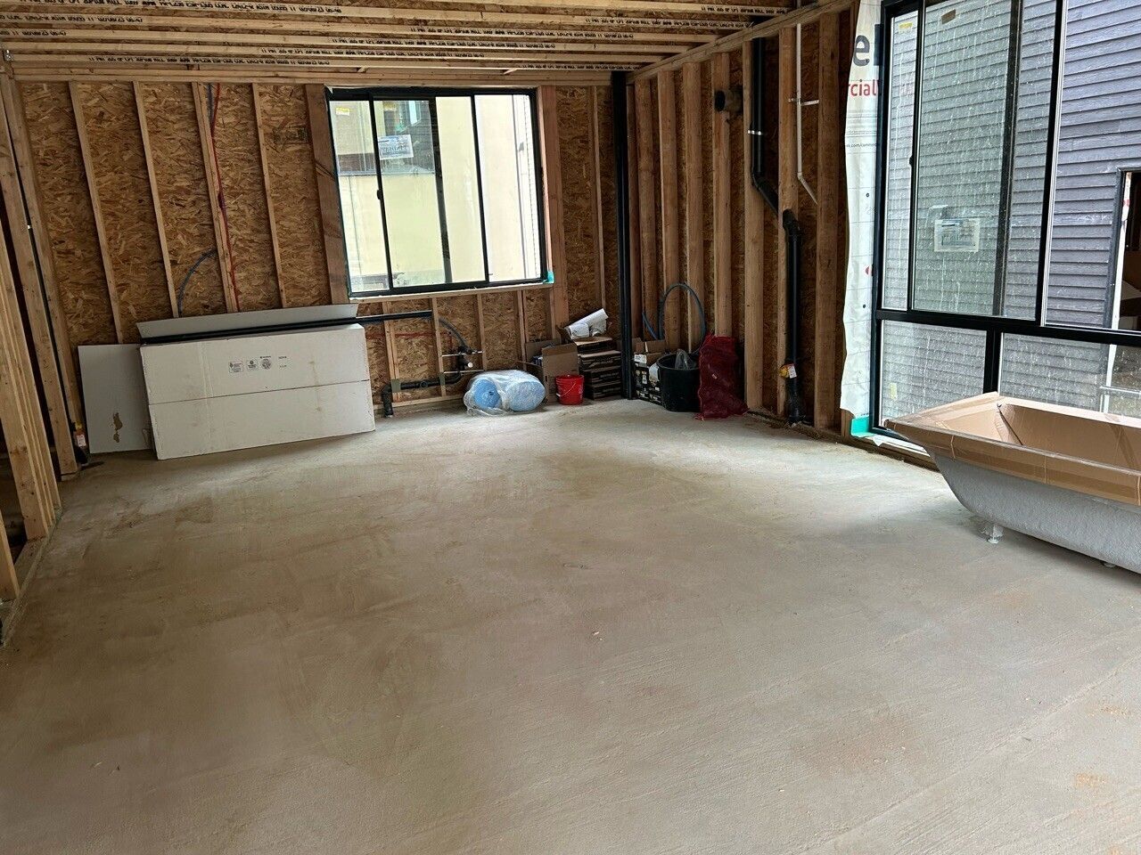 Unfinished room with exposed studs, a window, carpeted floor, and construction materials along the walls