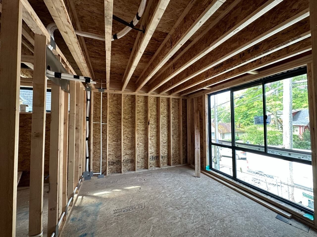 Unfinished room interior with exposed wood framing and large window wall letting in daylight.