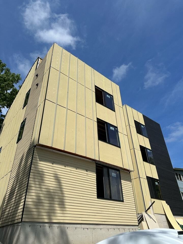 Low-rise beige apartment building under a blue sky with clouds, viewed from below.