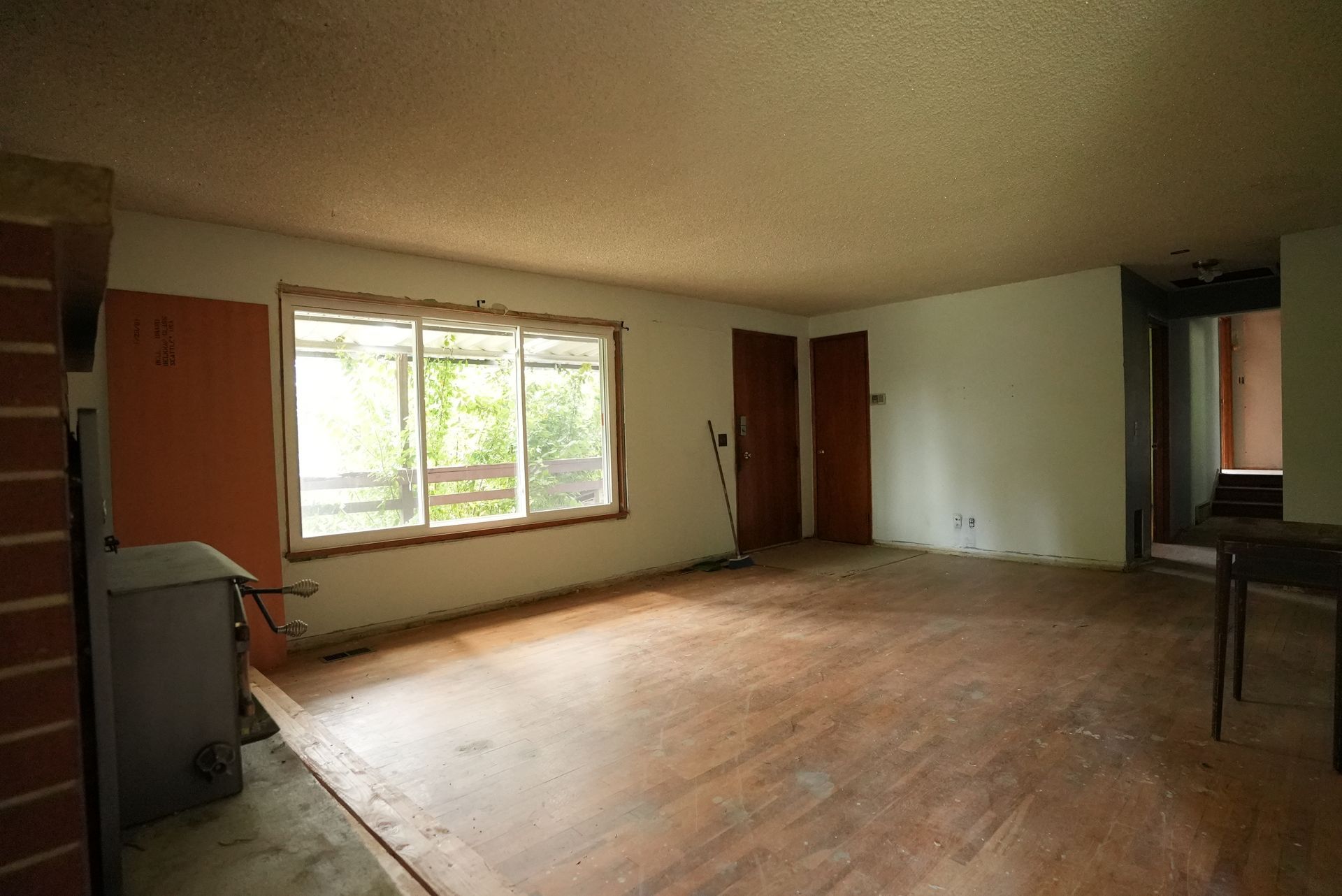 Empty living room with hardwood floors, large window, and doorway to another room