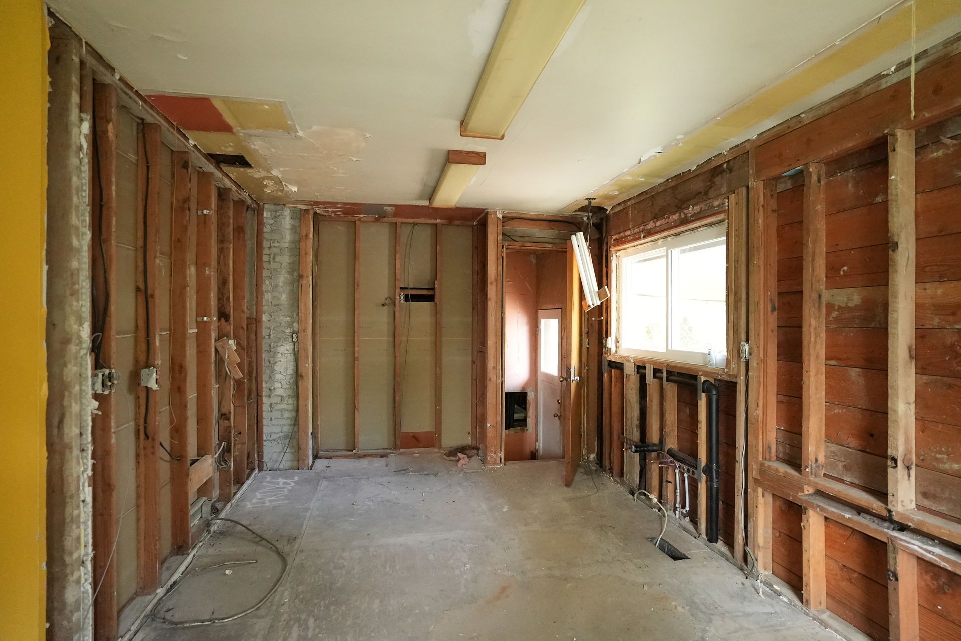 Bare room under renovation with exposed wooden studs, unfinished walls, and a window on the right.