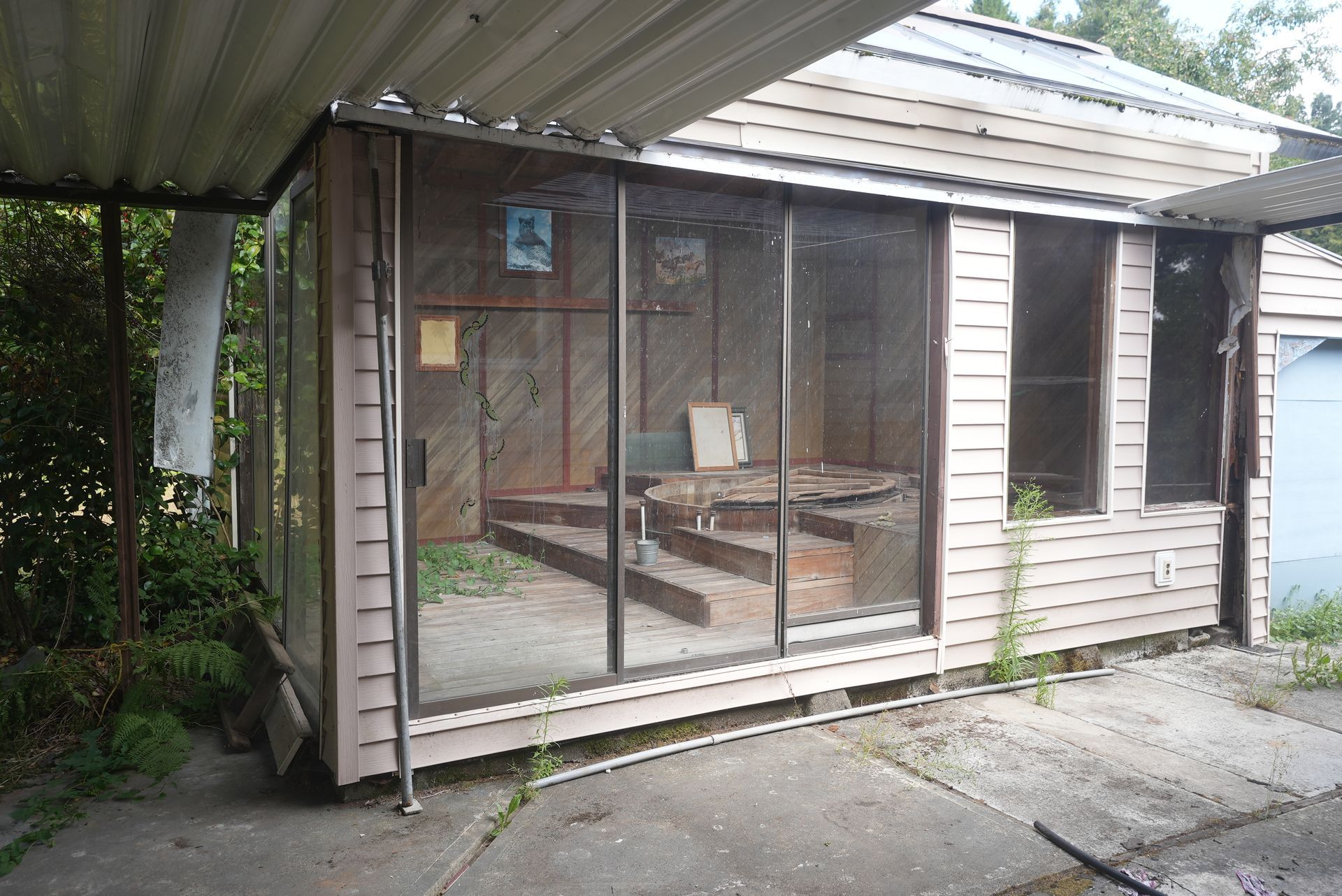 Old weathered wooden shed with wire-mesh enclosure and corrugated roof under a carport