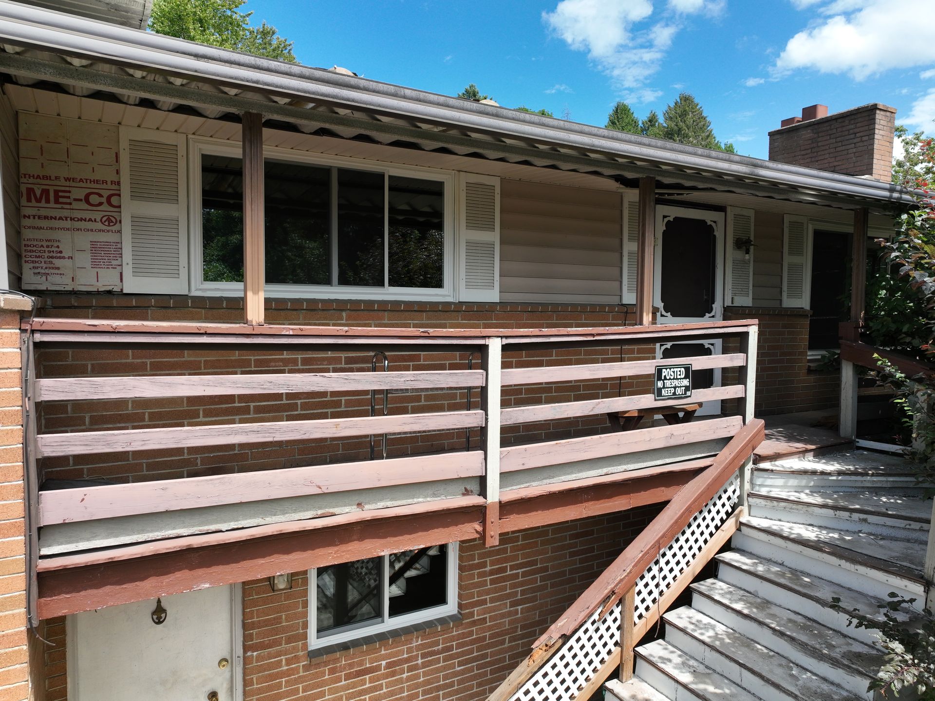 Exterior of a two-story house with a wooden balcony and stairs under a blue sky