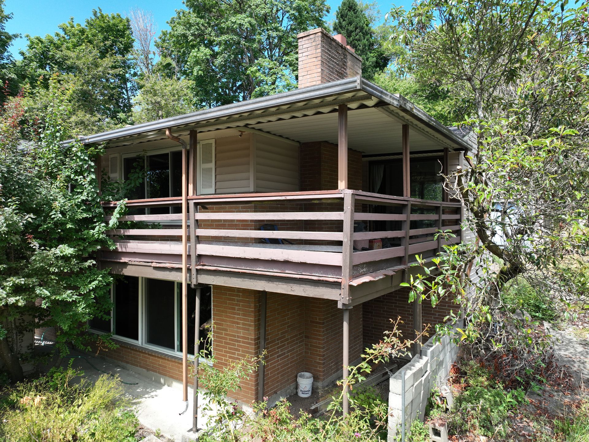 Two-story house with a wraparound porch, brick chimney, and dense trees surrounding it