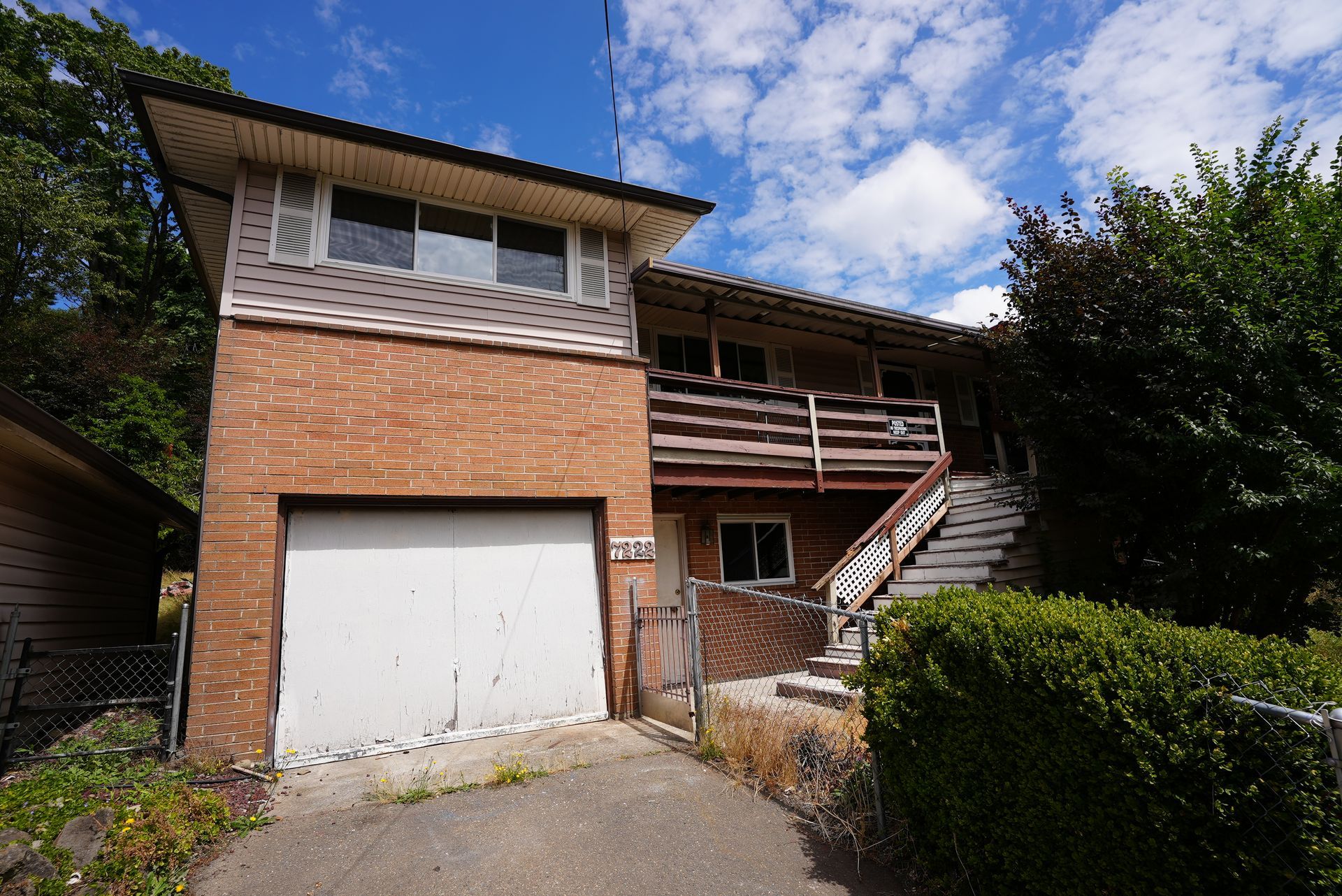 Two-story brick house with garage, exterior stairs, and a small front hedge under a blue sky.