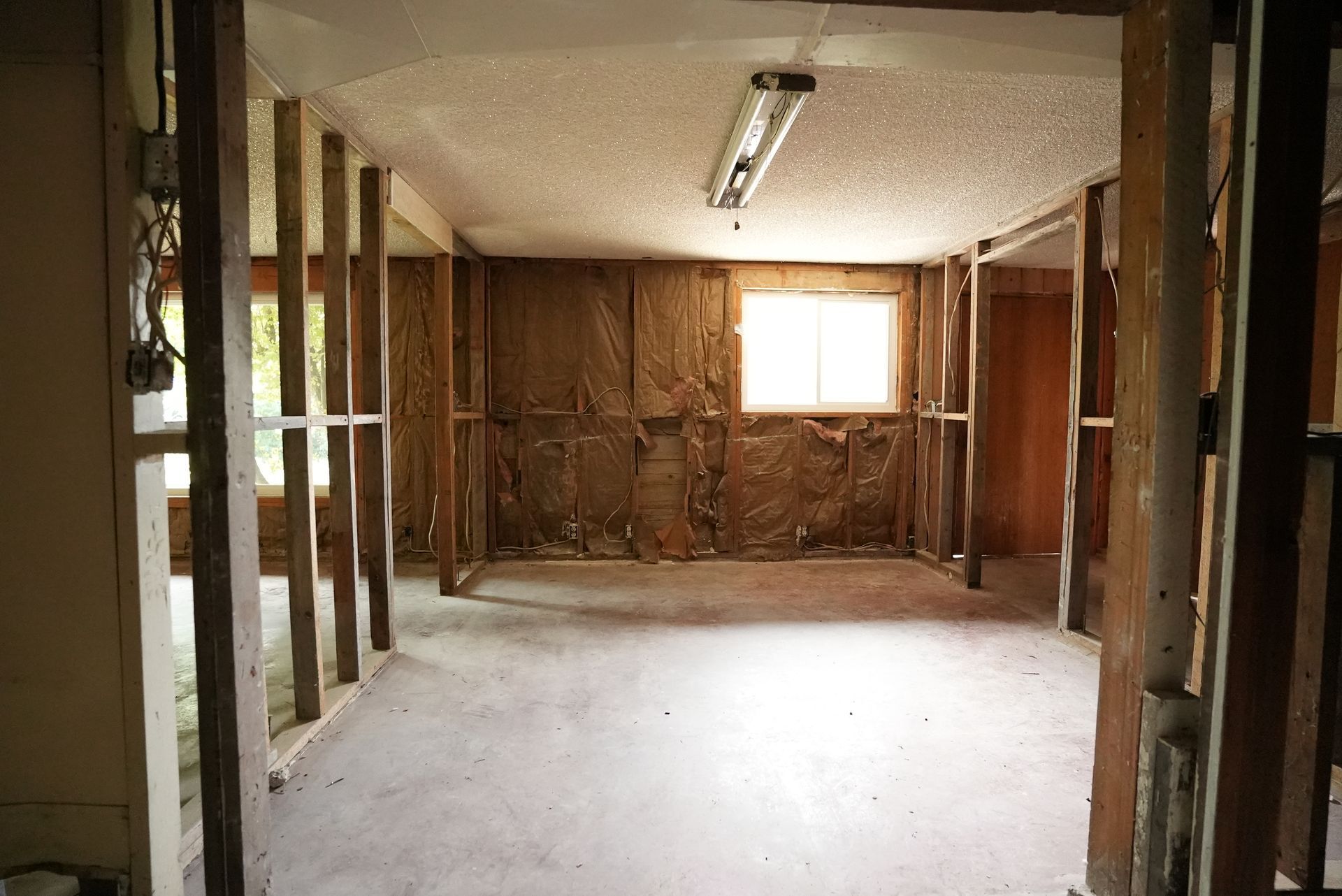 Empty unfinished room with exposed wall studs, bare floor, and a small window at the far end.