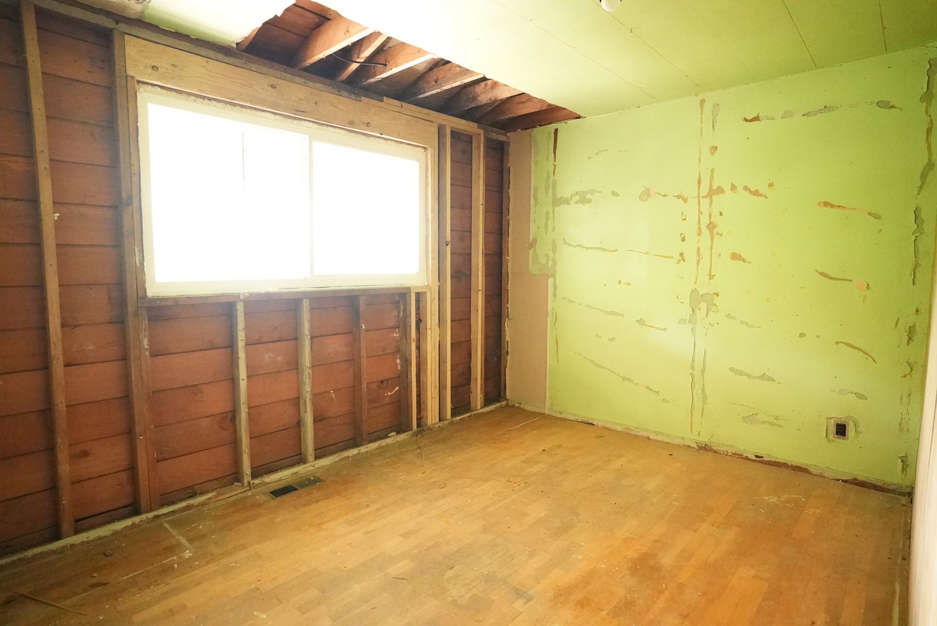 Empty unfinished room with exposed wall studs, green drywall, and a bright window.