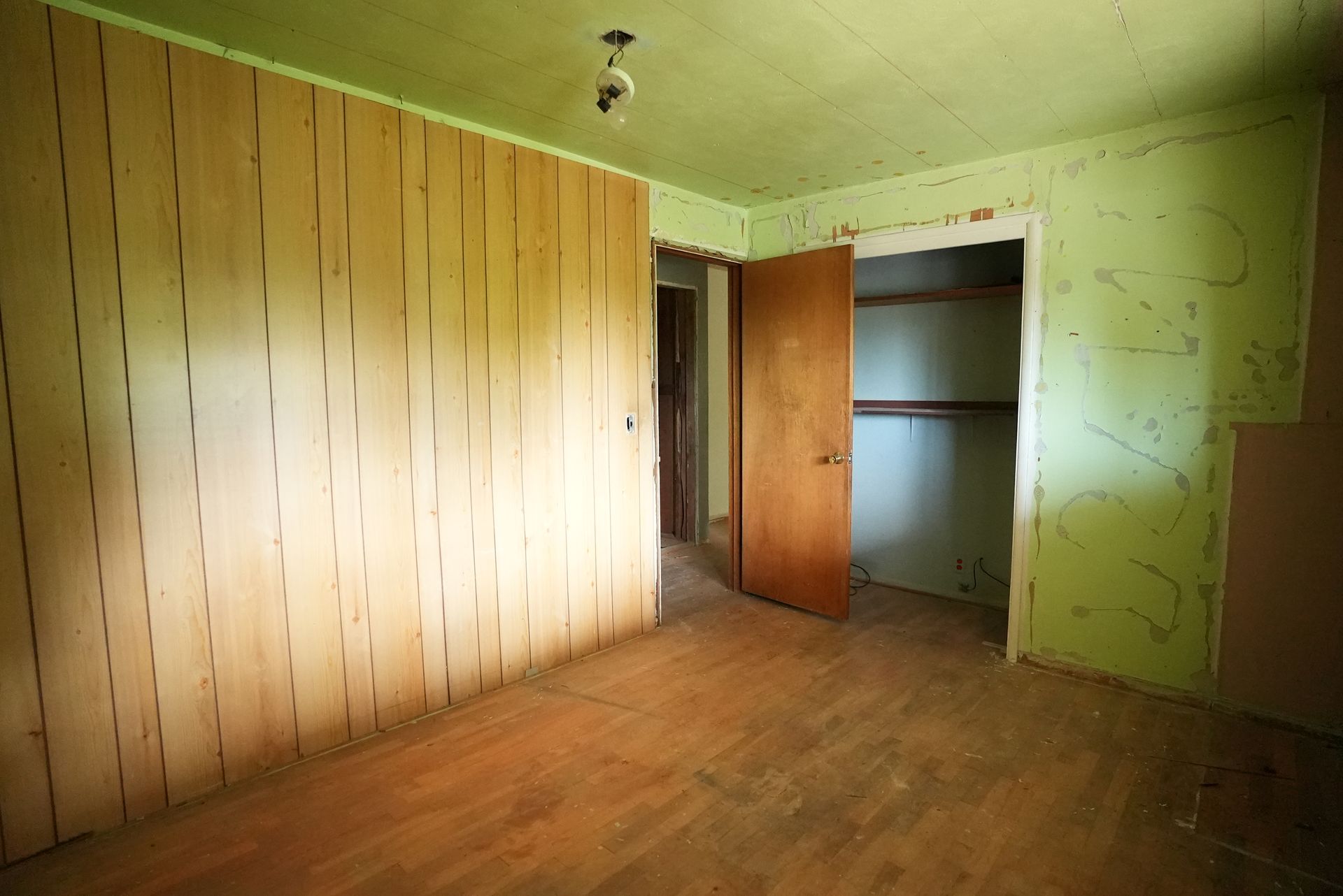 Empty room with wood-paneled walls, worn floor, and an open closet door.