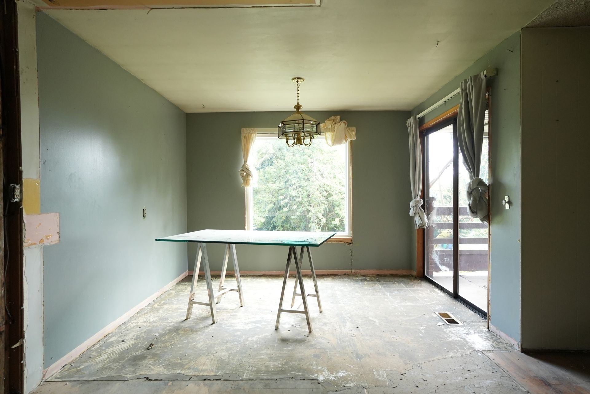 Empty dining room with pale green walls, a central window, and a table on sawhorses, under renovation.