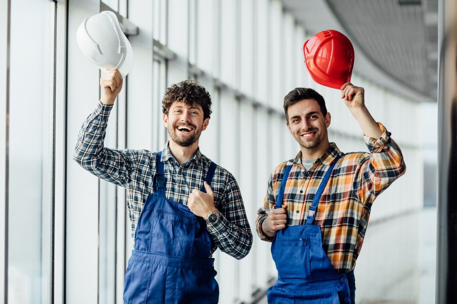 Two construction workers are standing next to each other holding hard hats and giving a thumbs up.