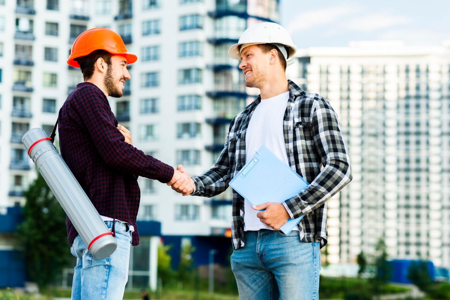 Two construction workers are shaking hands in front of a building.
