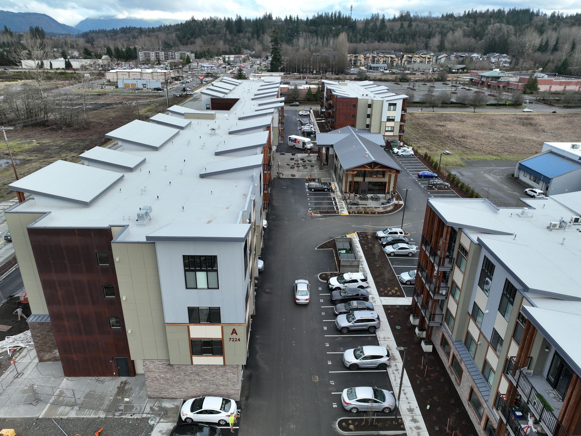 Aerial view of a snowy residential complex with parked cars and mountains in the distance.