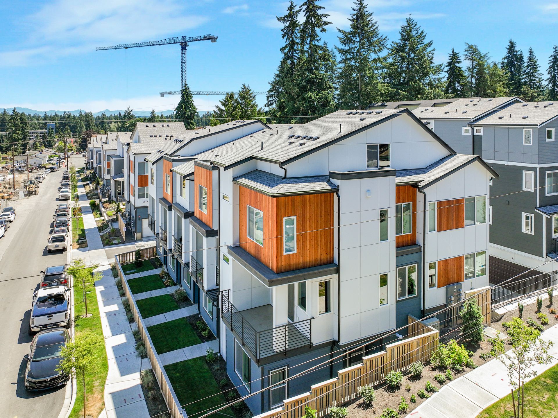 Row of modern townhomes along a street, with a construction crane and trees in the background.
