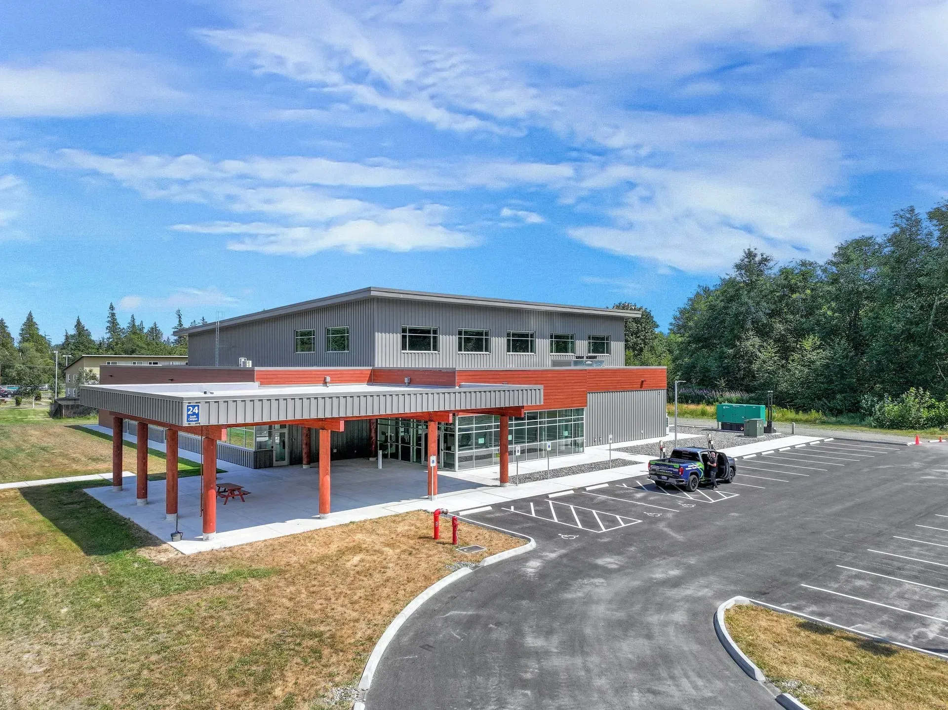 Modern two-story building with red columns, parking lot, and a partly cloudy blue sky