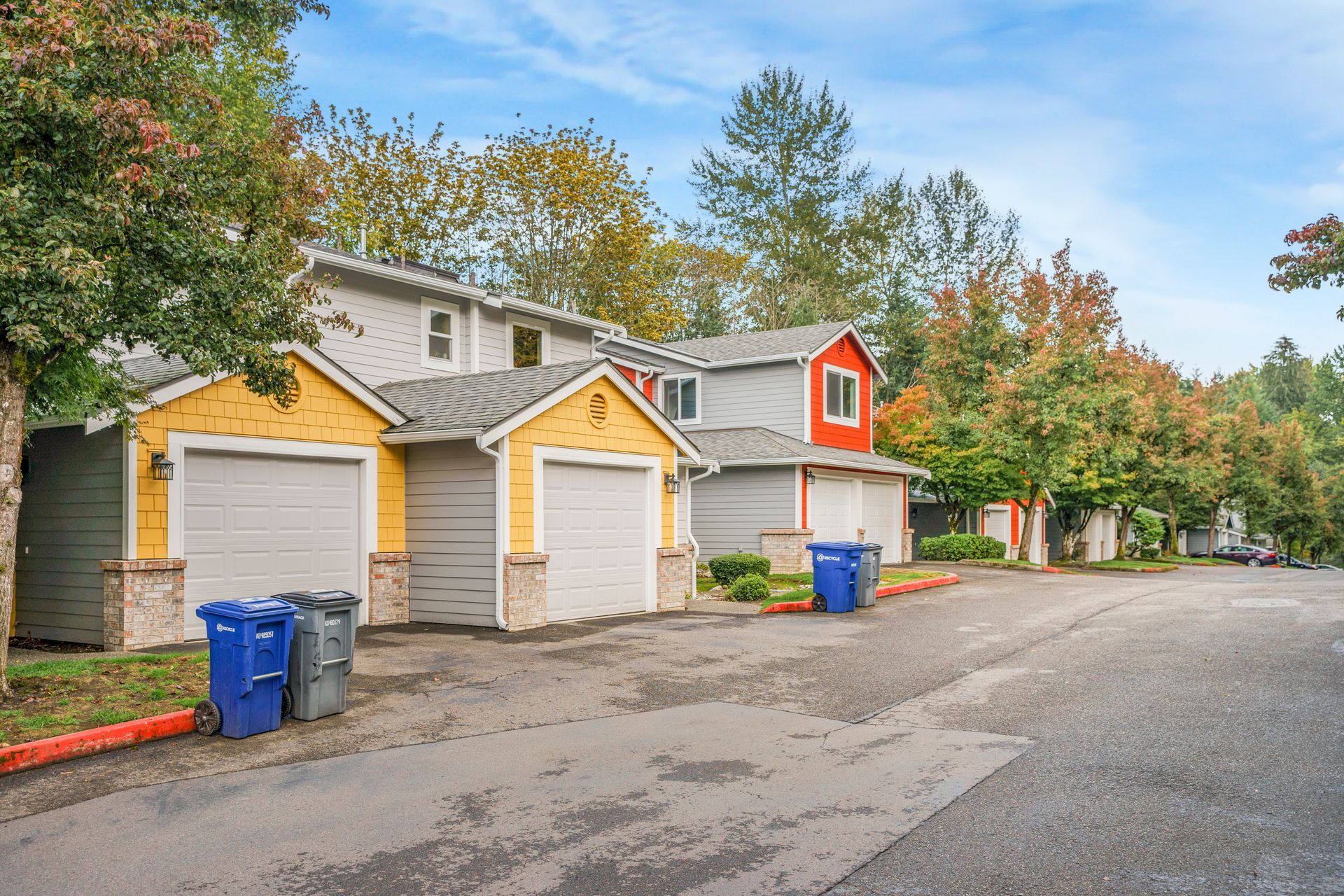 A row of houses with garages and trash cans in front of them.