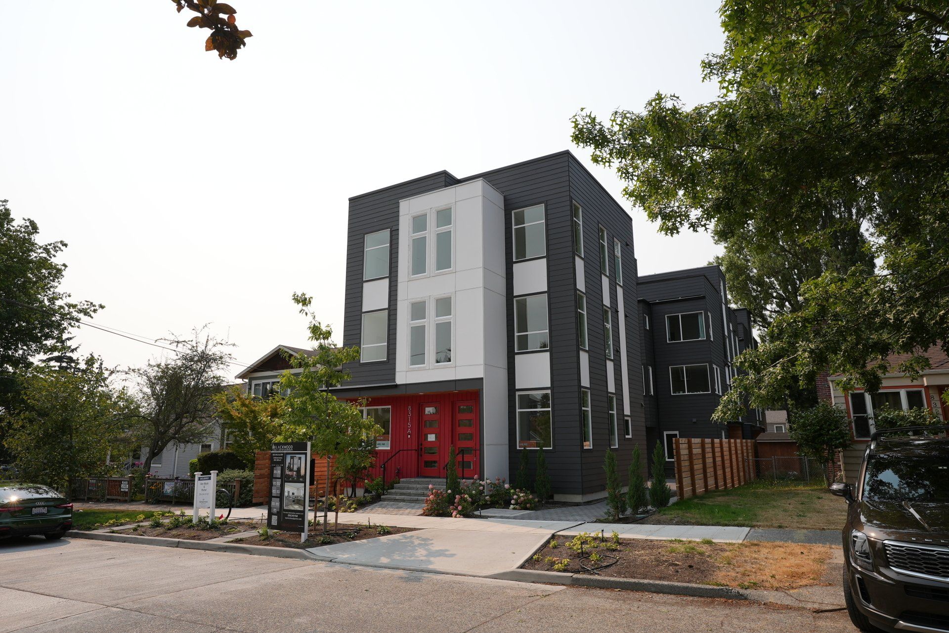A black and white building with a red door and a black car parked in front of it