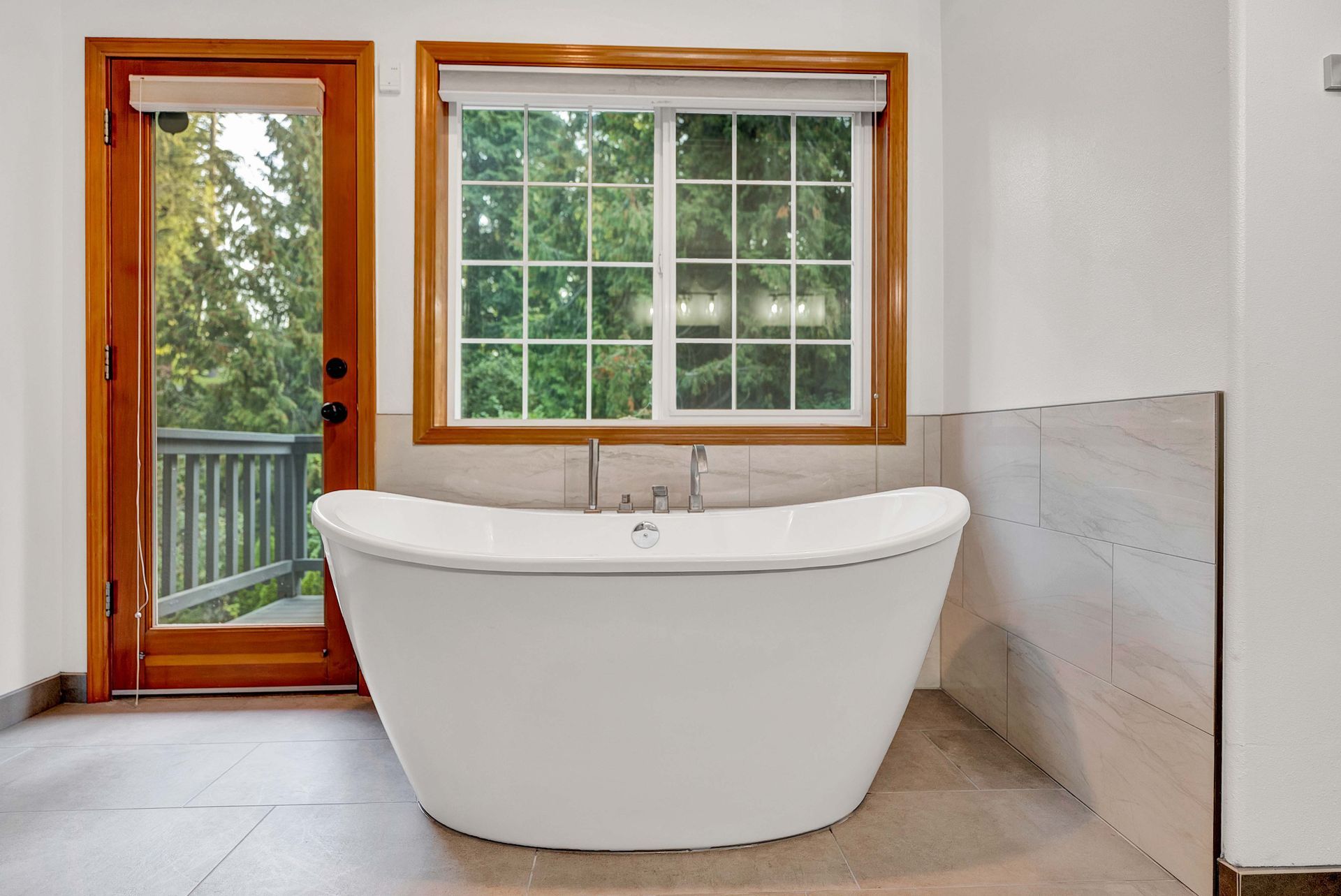 A bathtub in a bathroom next to a window and a door.
