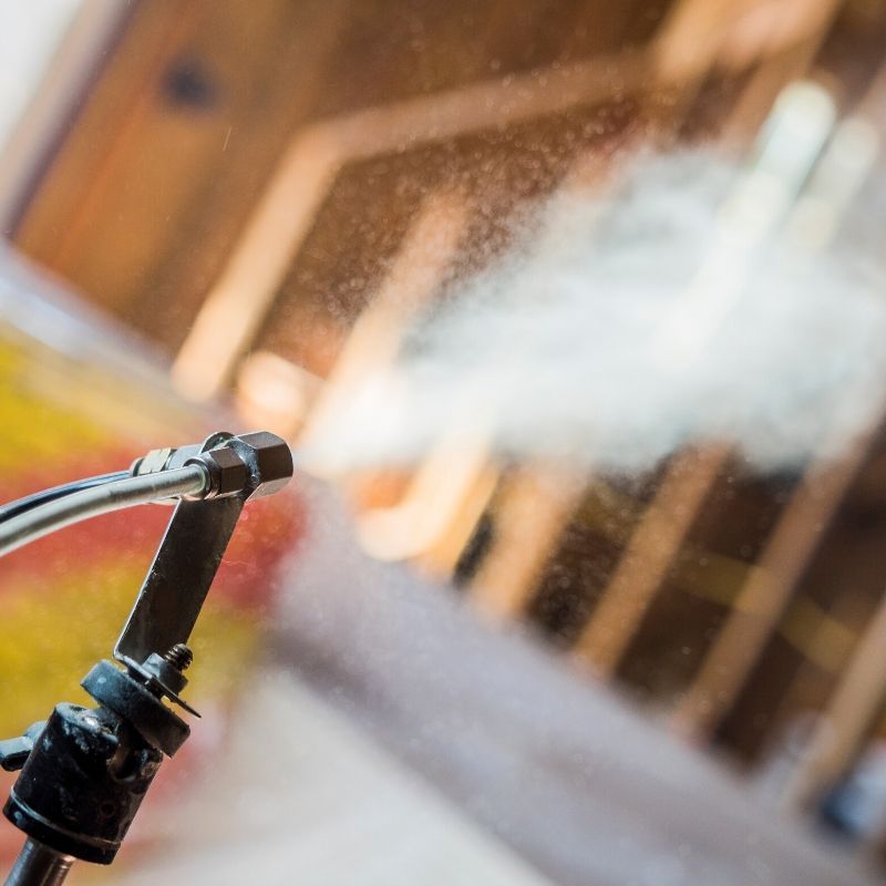 A pressure washer spraying water mist across a wooden outdoor surface.