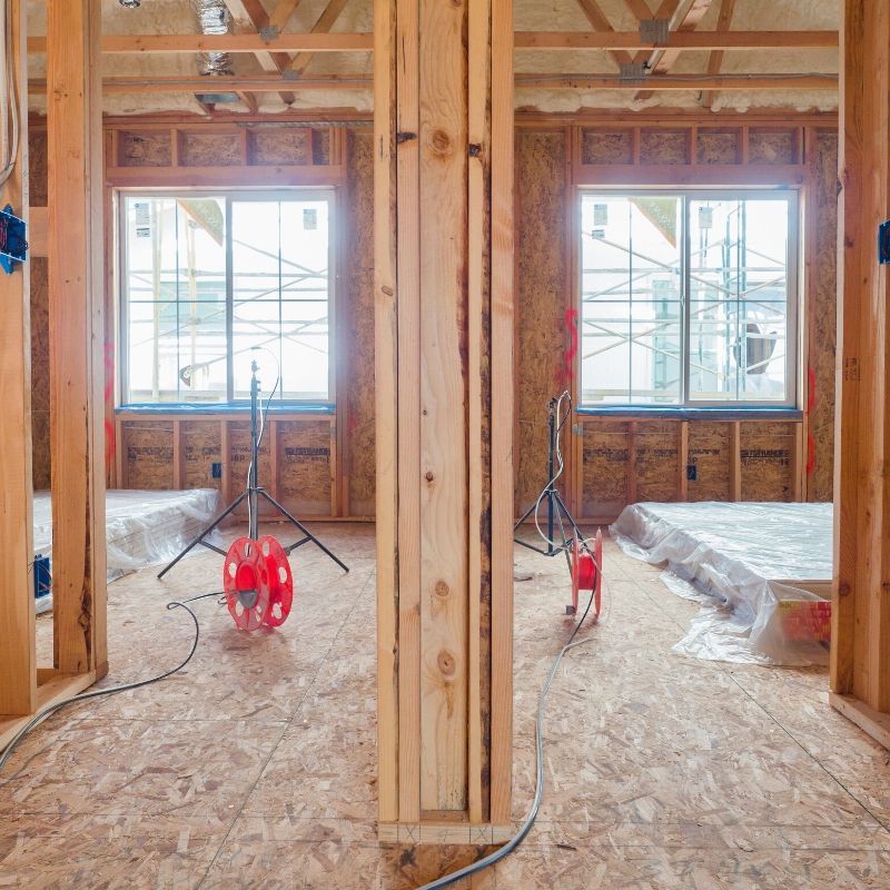 Interior of a framed room under construction, with exposed wood studs, windows, and a red extension cord reel.