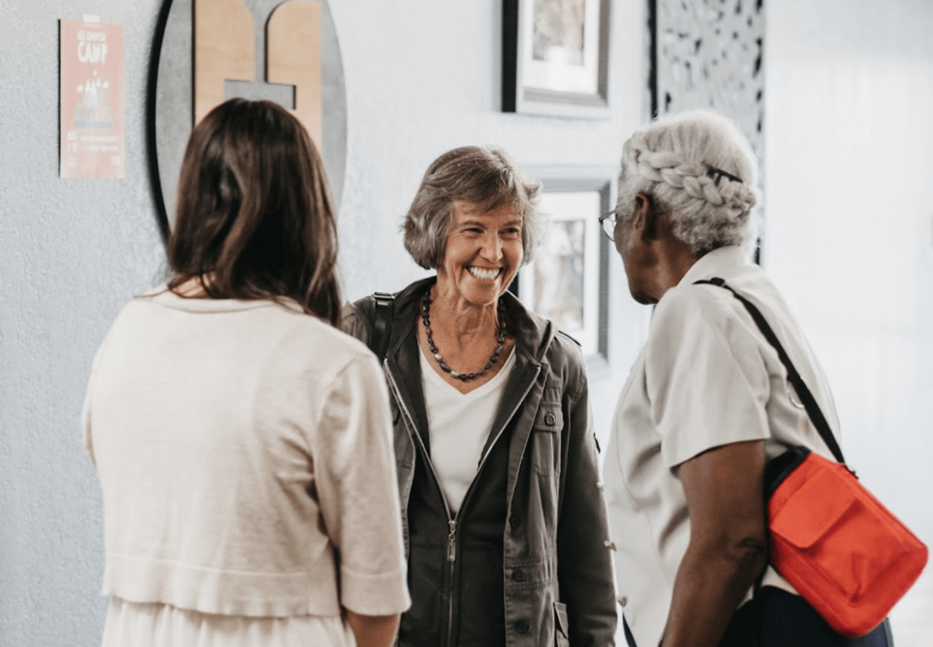 Three women are talking to each other in a hallway.