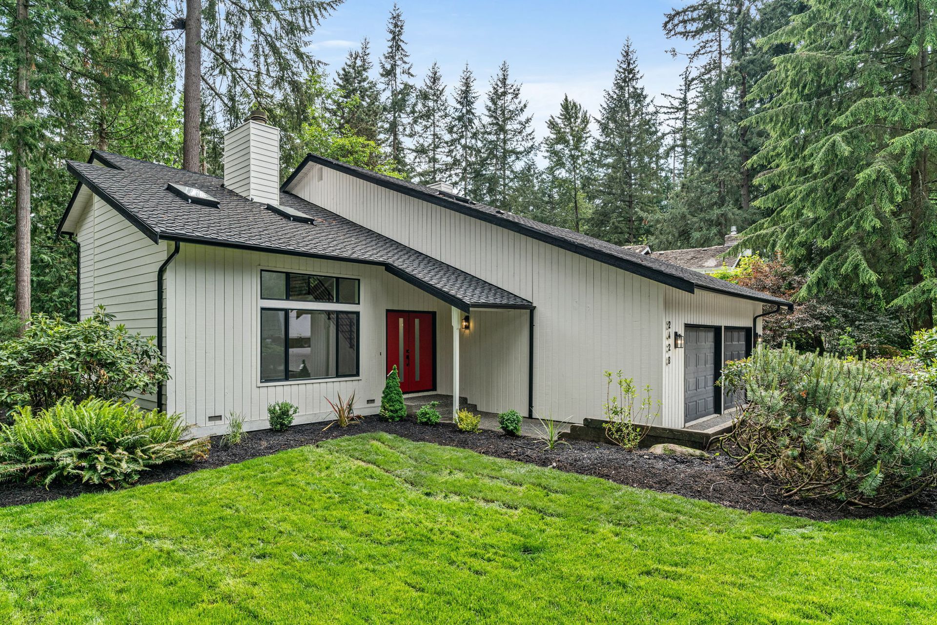 A white house with a red door is surrounded by trees.