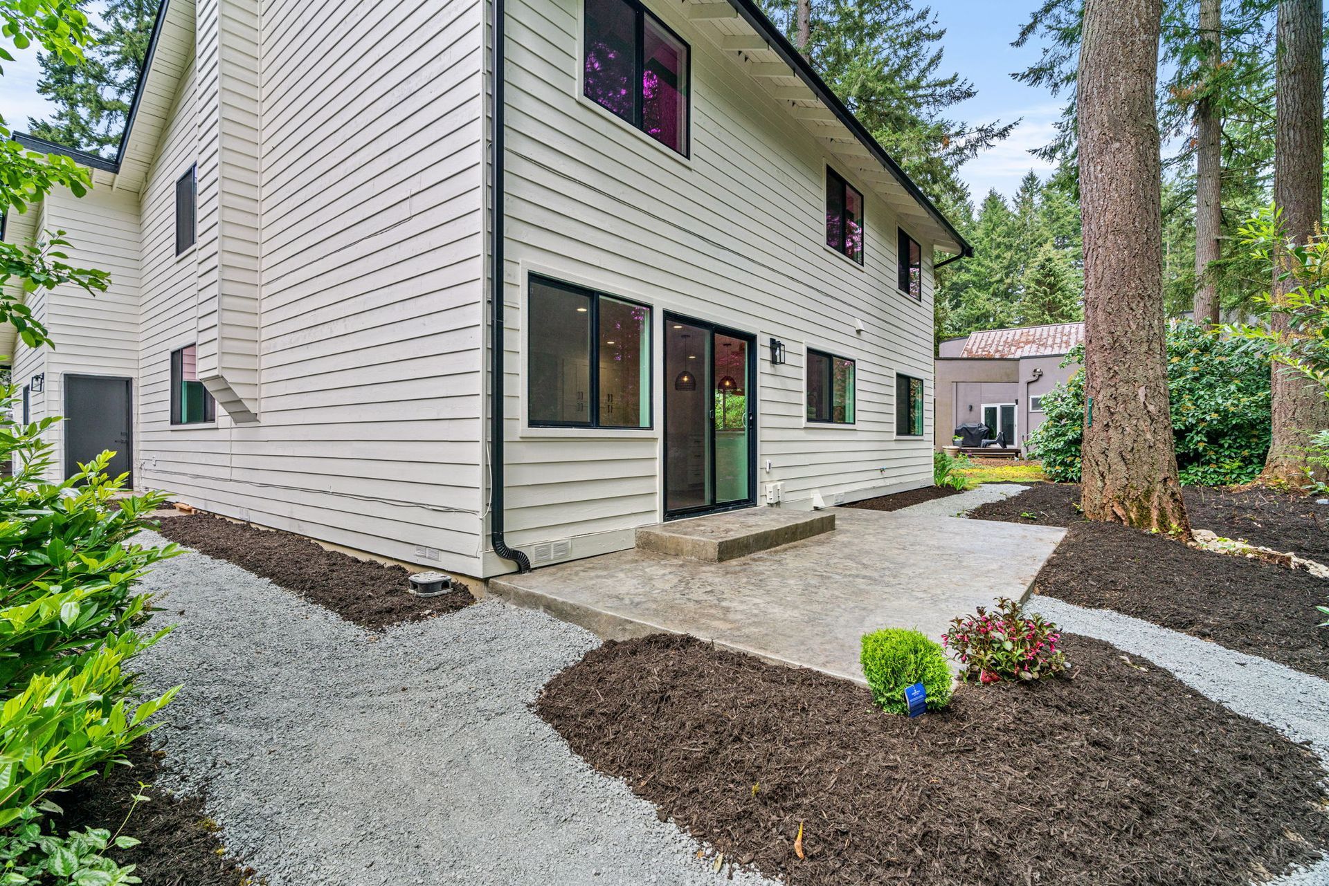 A white house with a patio in front of it is surrounded by trees.