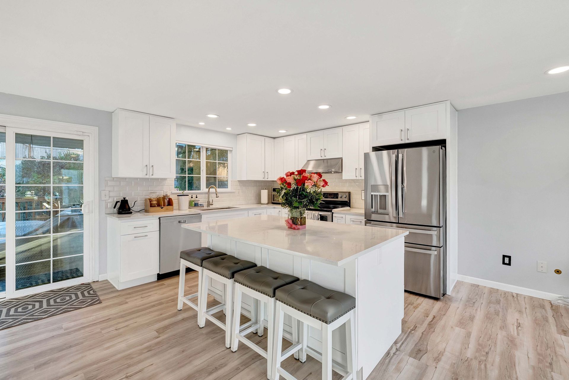 Bright modern kitchen with white cabinets, island seating, stainless steel fridge, and large windows