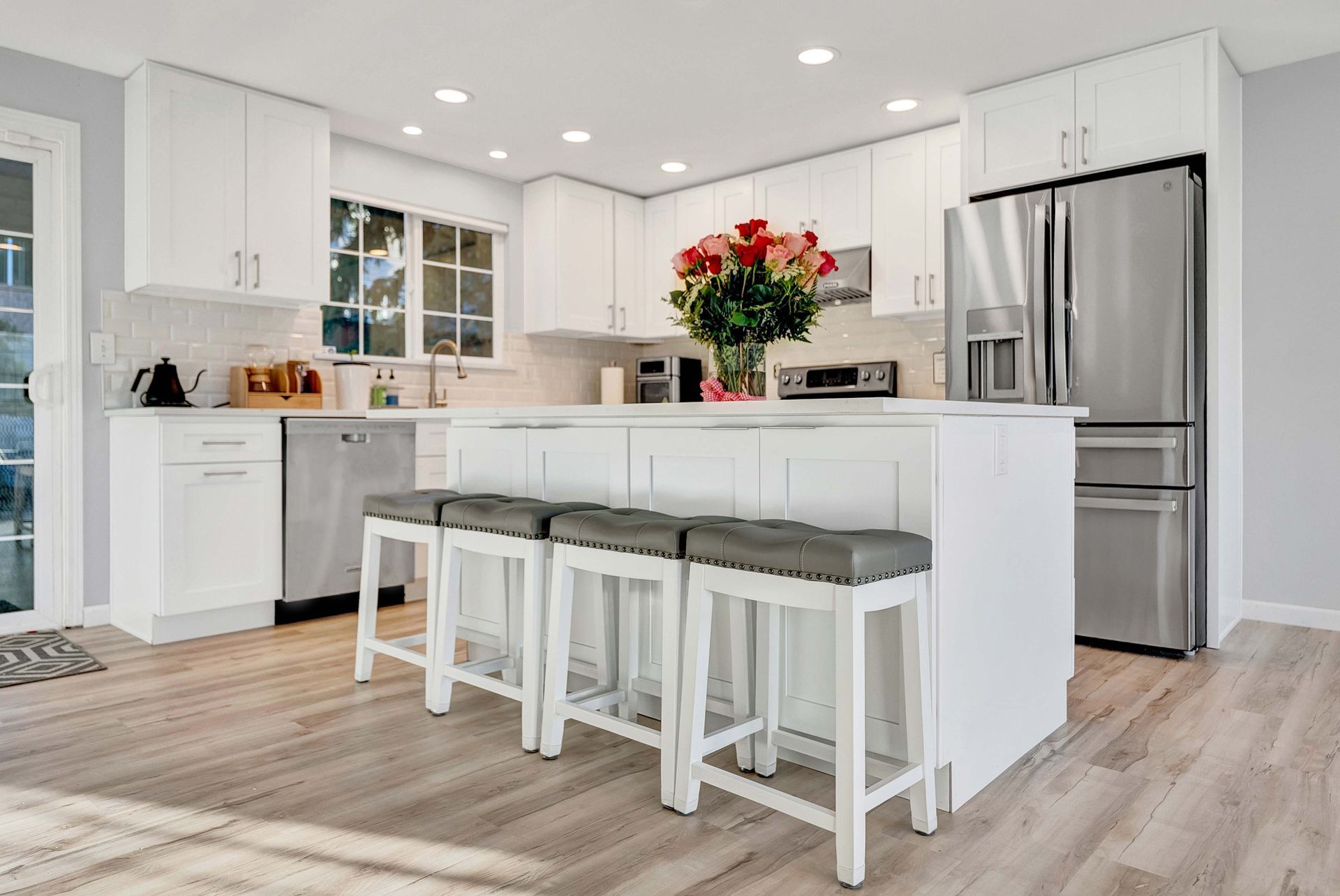 Bright white kitchen with island, stools, stainless steel appliances, and red flowers on the counter