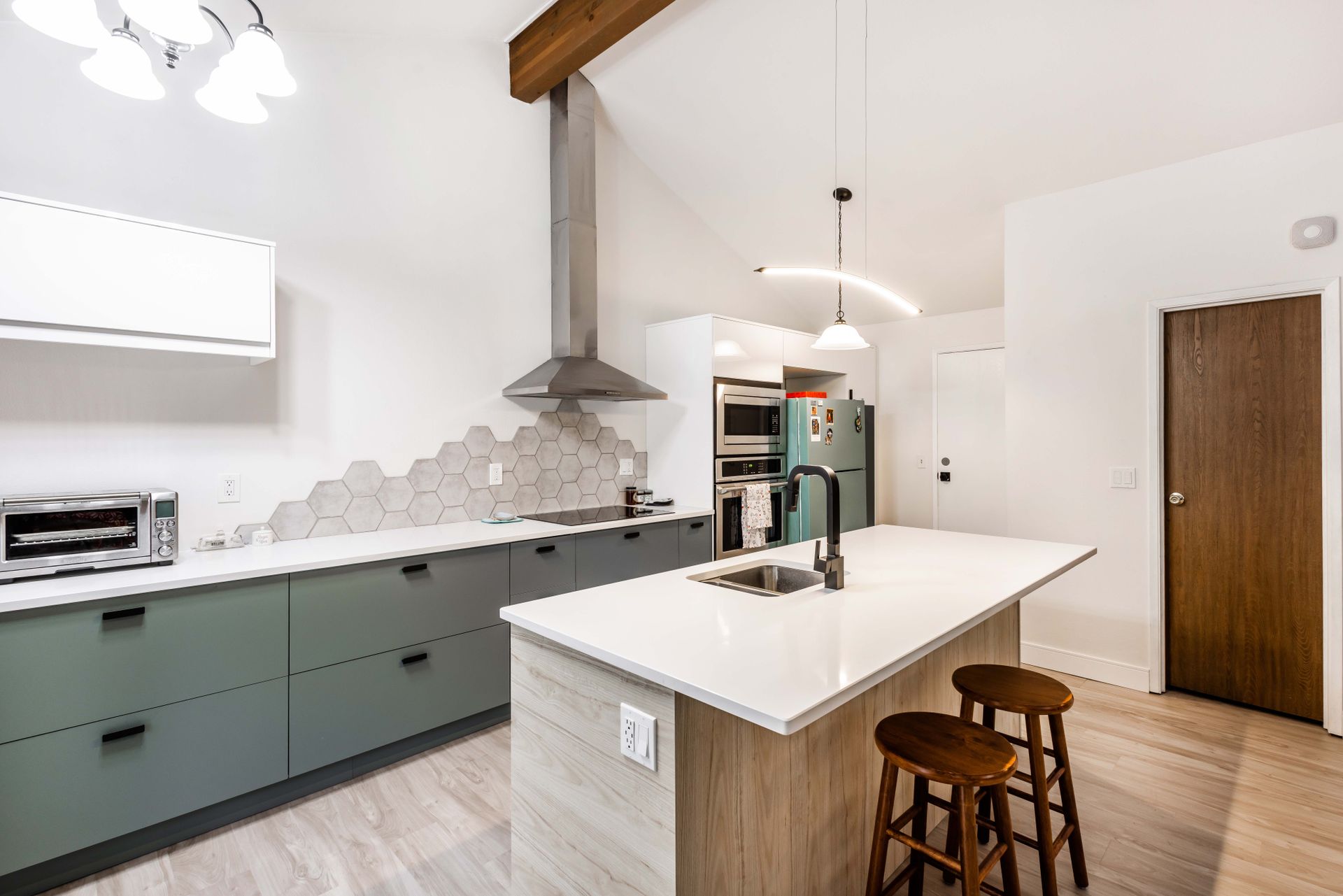 Modern white kitchen with island, sage cabinets, wood stools, and stainless range hood