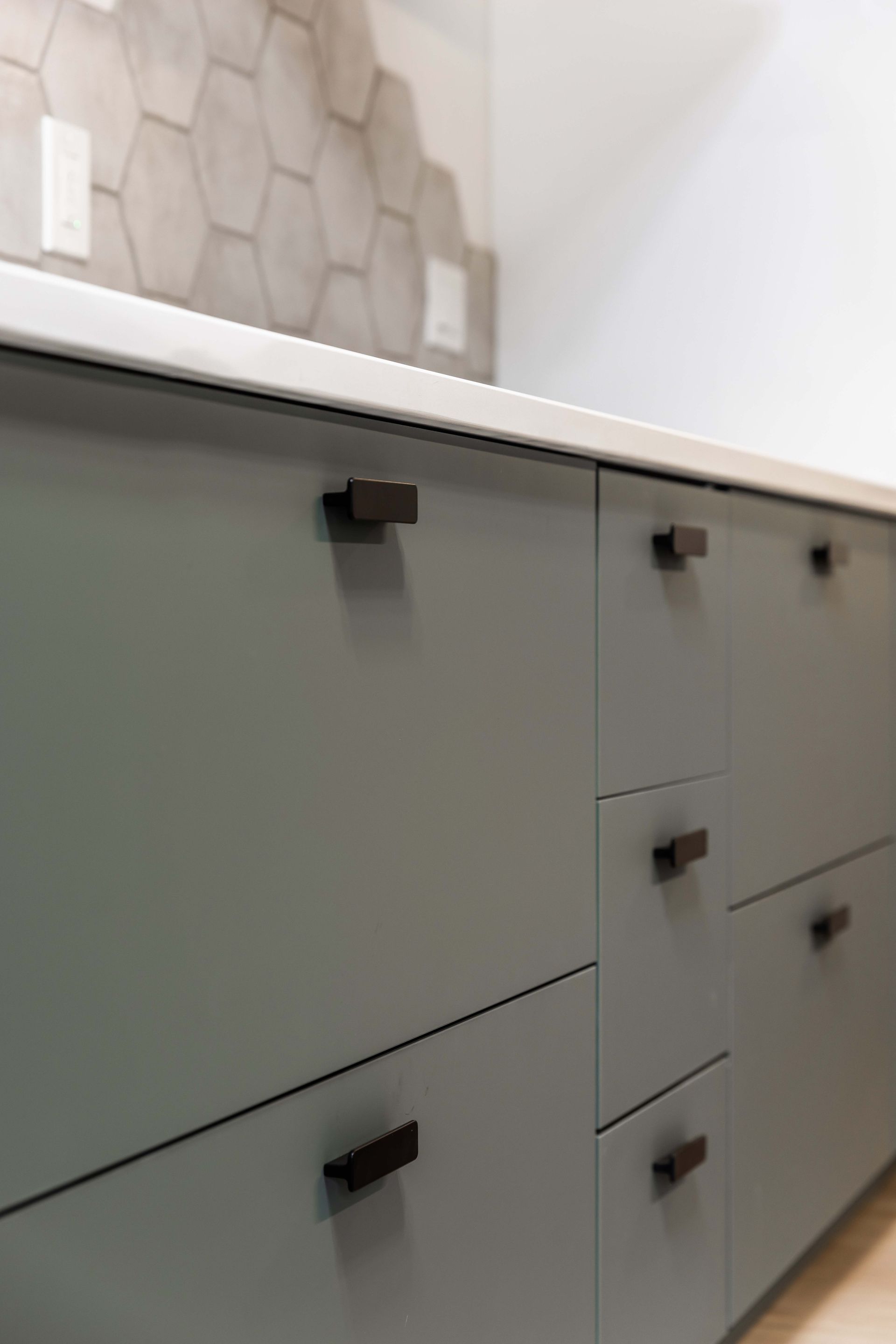 Gray bathroom vanity with black handles and hexagon tile backsplash