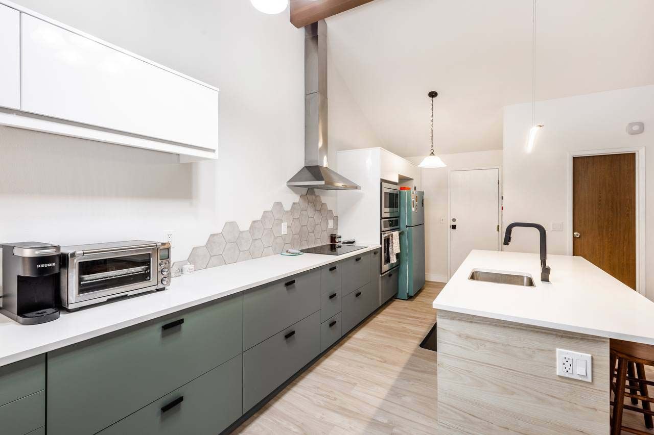 Modern kitchen with white island, green cabinets, stainless range hood, and patterned backsplash