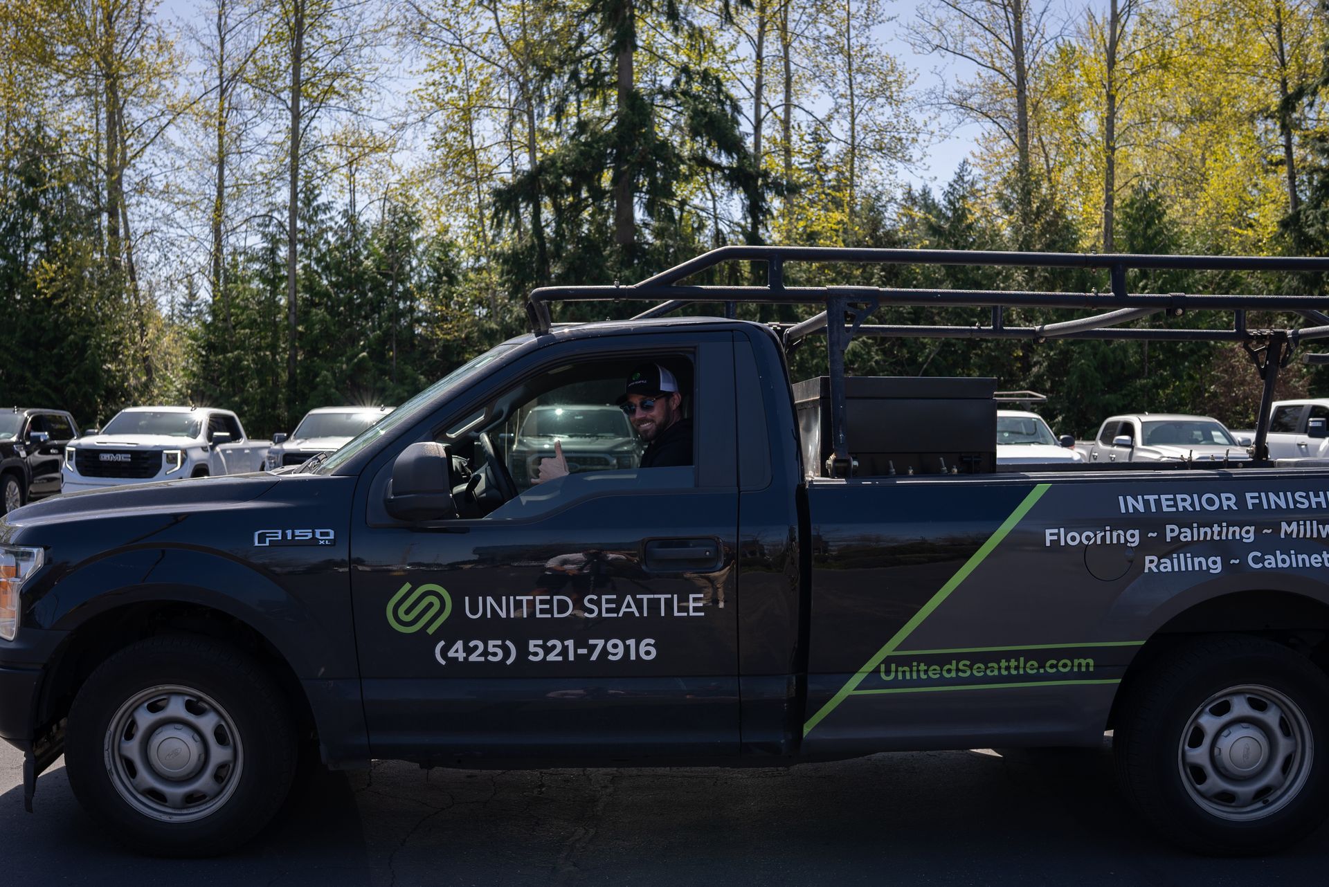 Black utility truck with ladder rack and company logos parked outdoors by trees