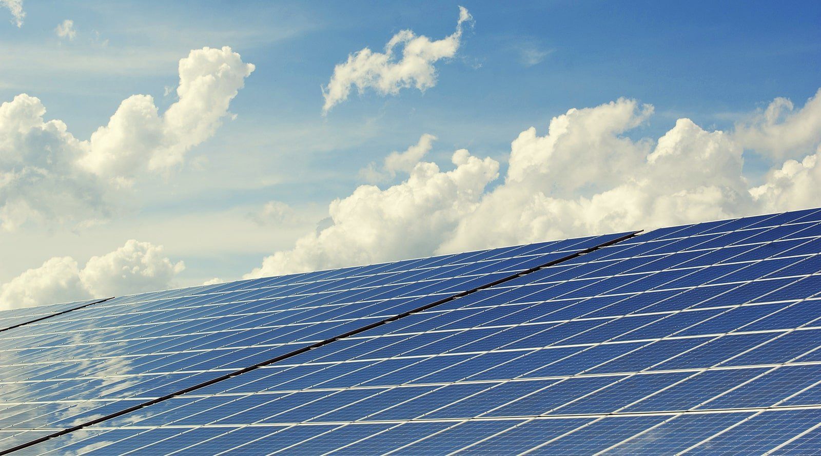 A row of solar panels against a blue sky with clouds.