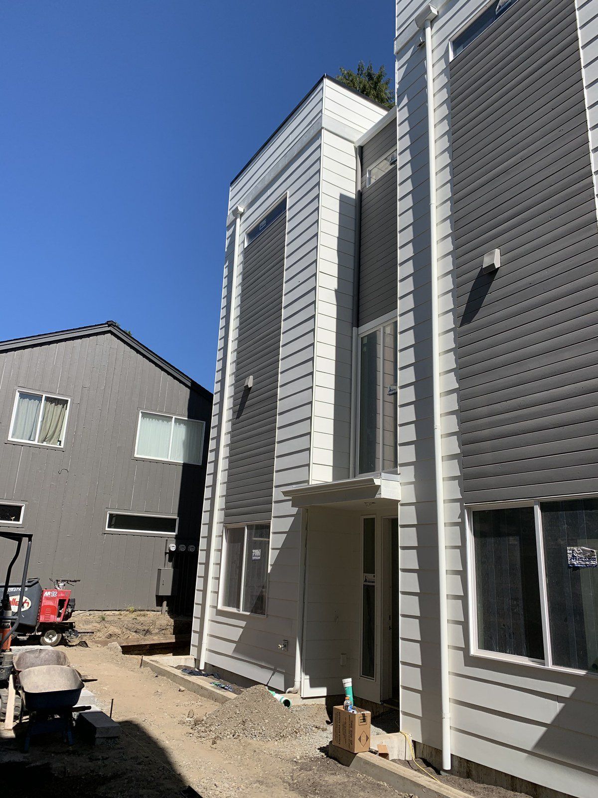 New gray house with vertical siding under construction beside neighboring homes on a sunny day