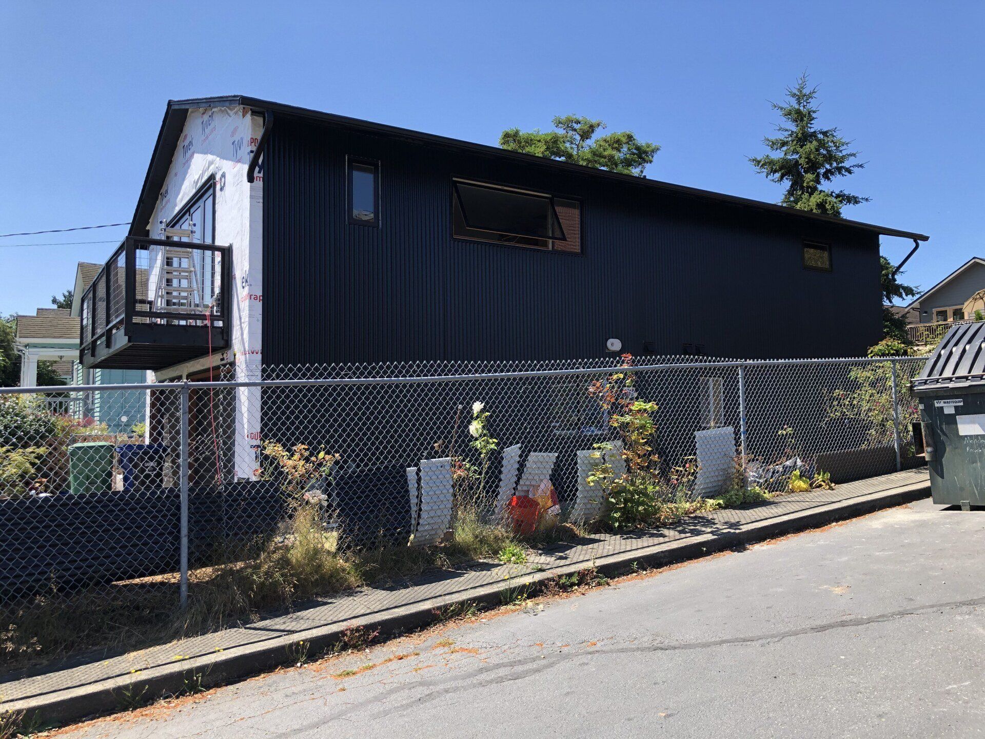 A black house with a balcony is behind a chain link fence.