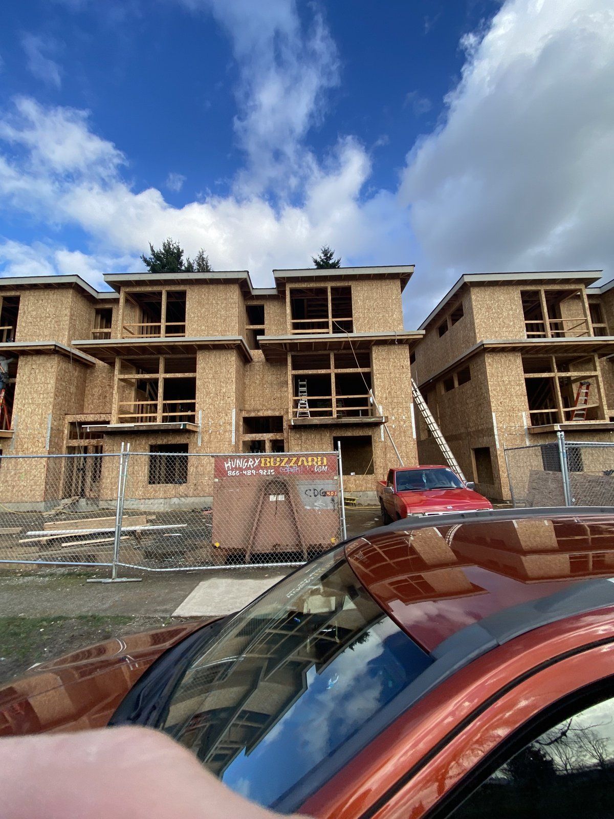 A red car is parked in front of a building under construction.