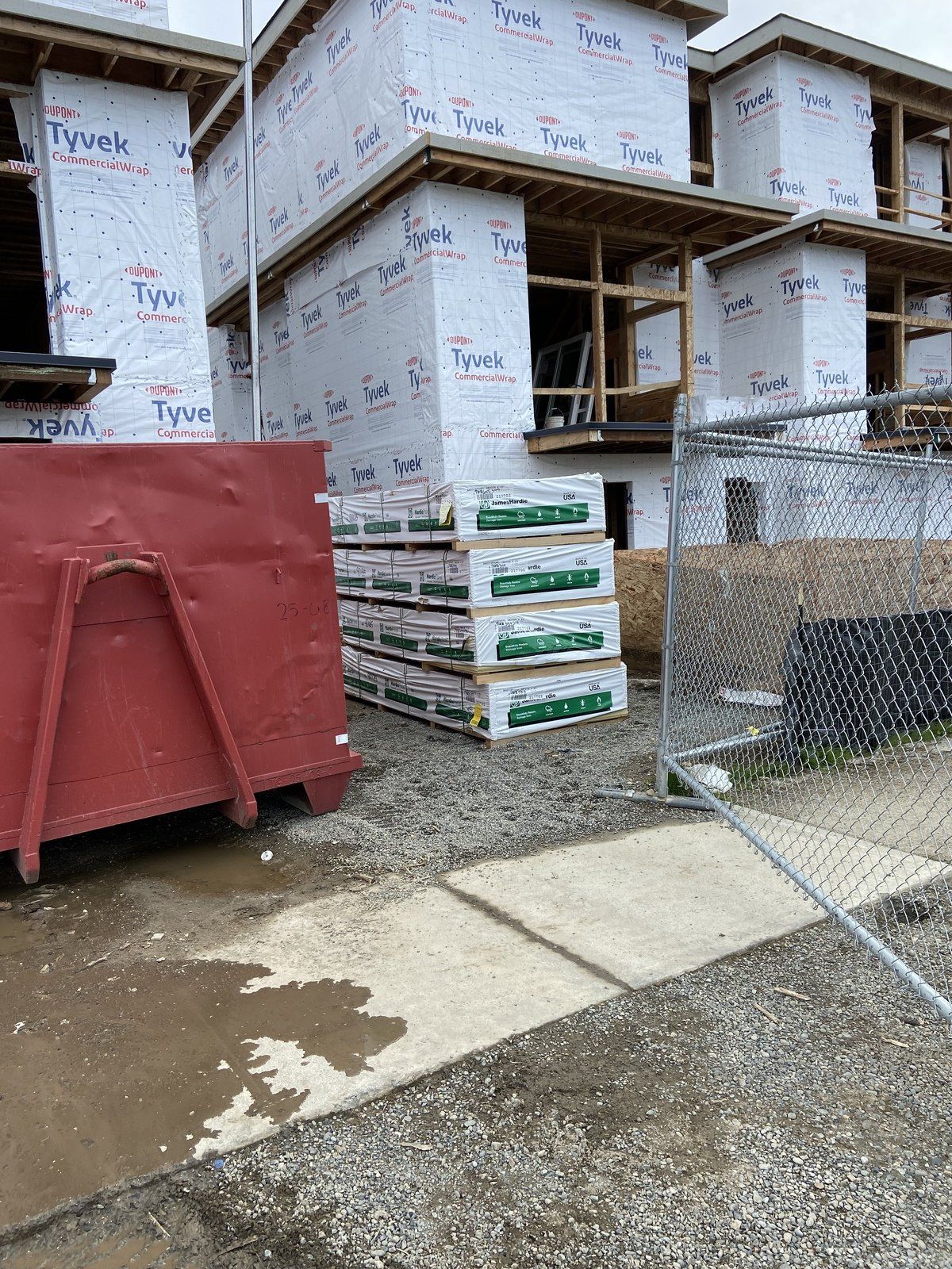 A red dumpster is sitting in front of a building under construction.