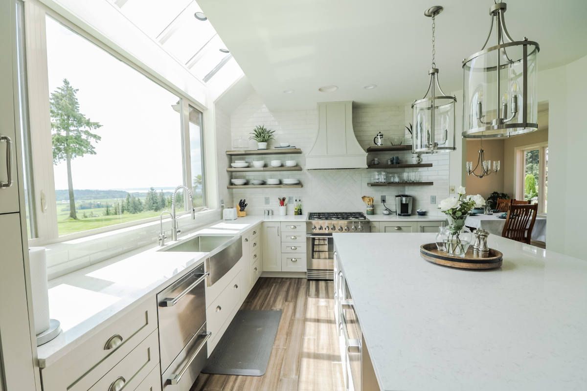 A kitchen with white cabinets and stainless steel appliances and a large window.