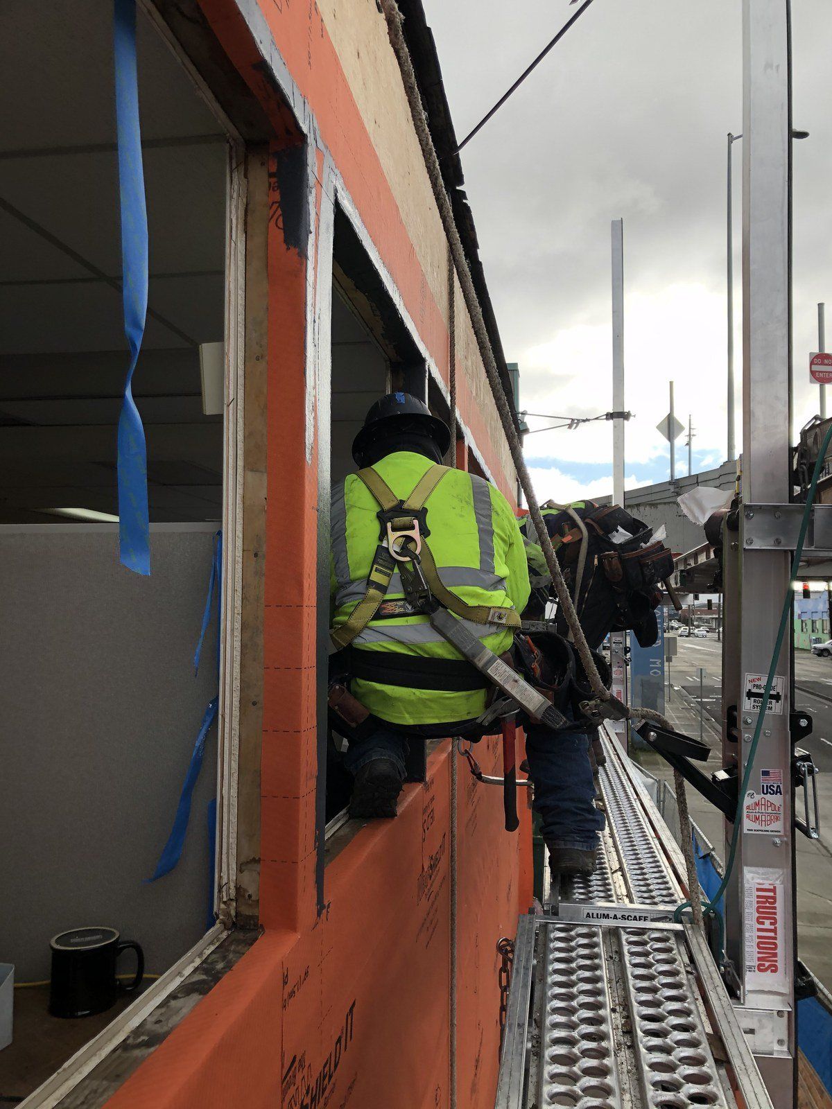Worker in neon jacket stands on scaffolding beside an orange building during construction.
